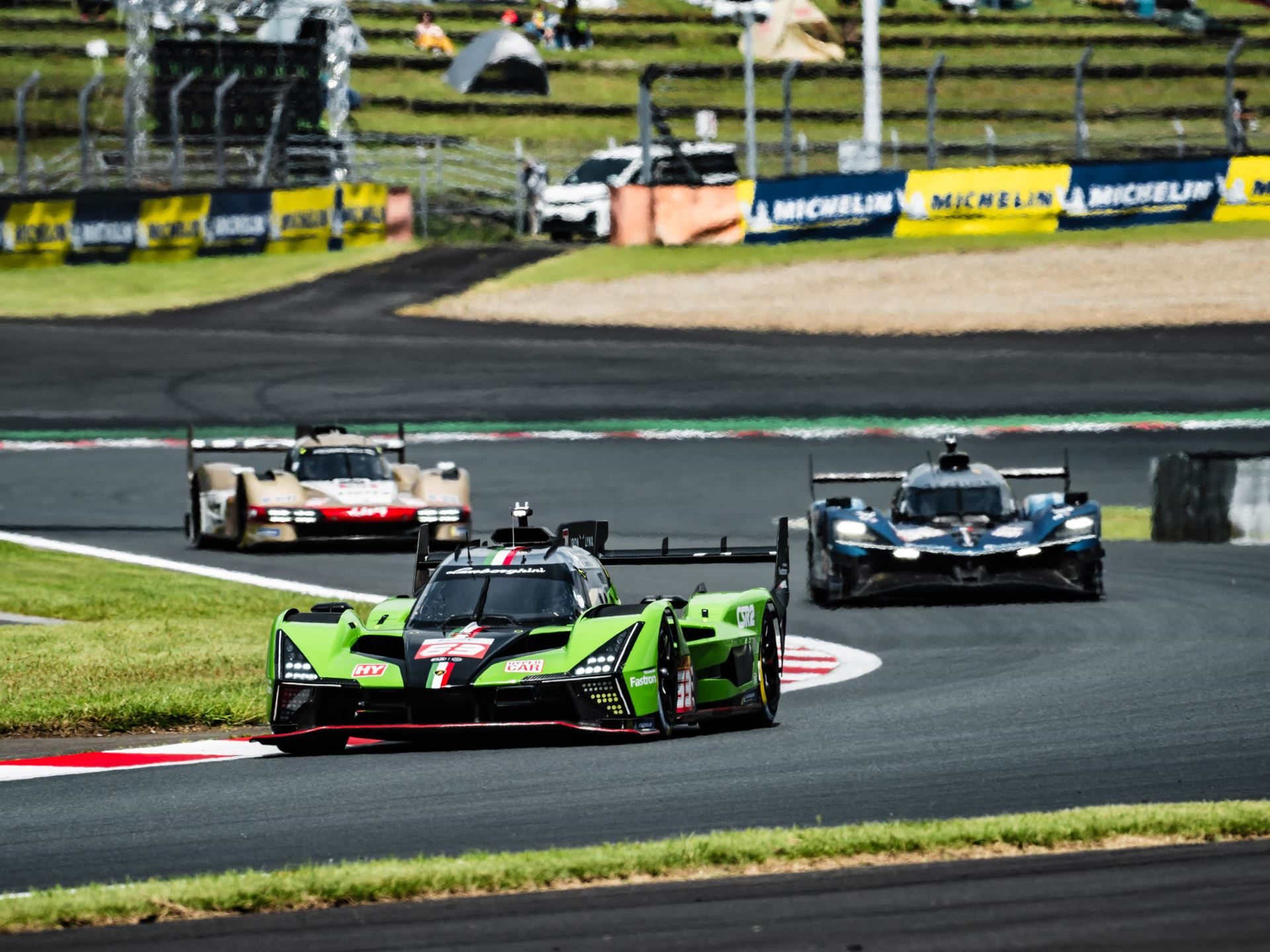 Lamborghini Sc63 Earns First Hyperpole At Fuji, Then A Drivetrain Failure Ends The Story Early 3 Green lamborghini sc63 leading two other prototype race cars on the fuji speedway circuit with spectators visible in the grandstands