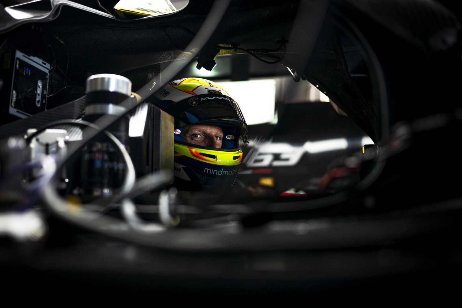 Close-up of a race driver's eyes visible through a colorful helmet visor inside the Lamborghini SC63 cockpit, with the number 63 on the helmet