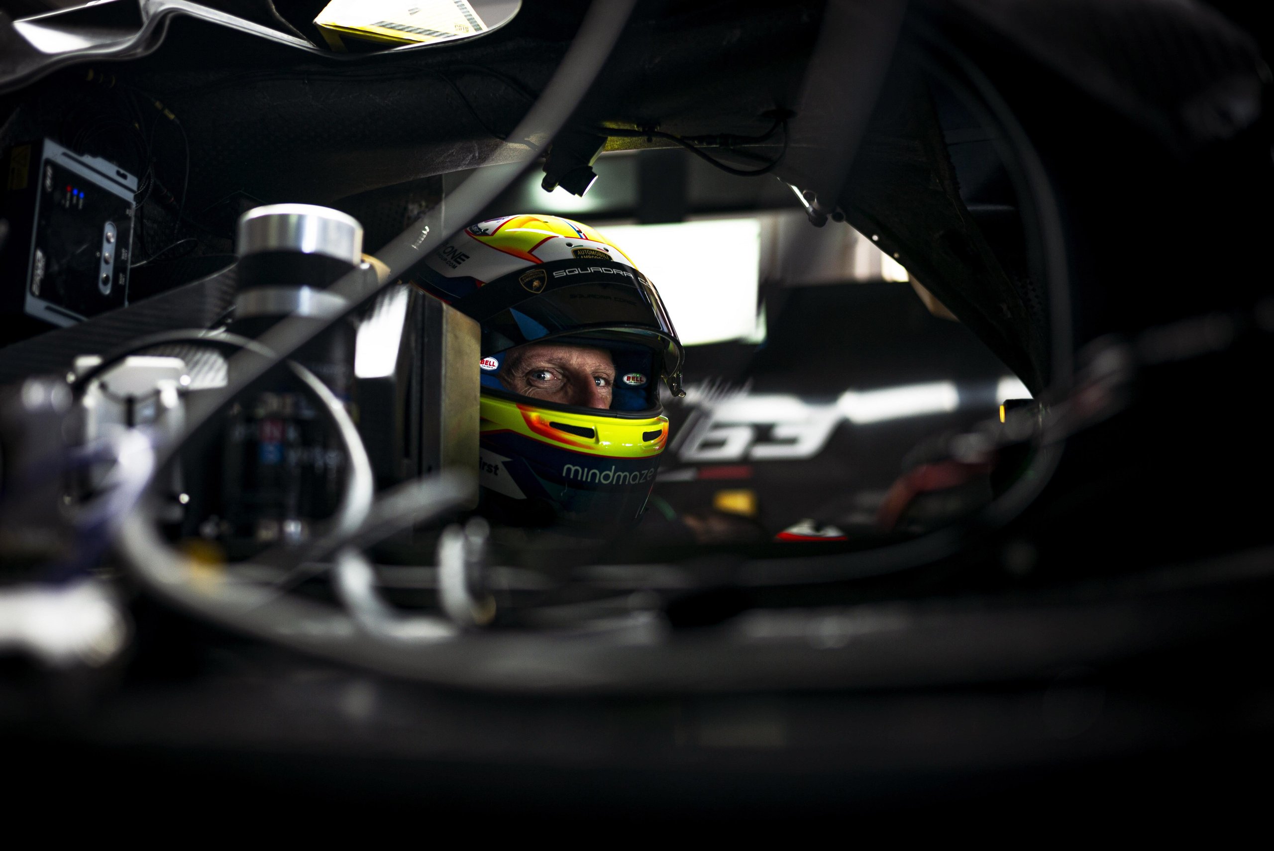 Close-up of a race driver's eyes visible through a colorful helmet visor inside the lamborghini sc63 cockpit, with the number 63 on the helmet