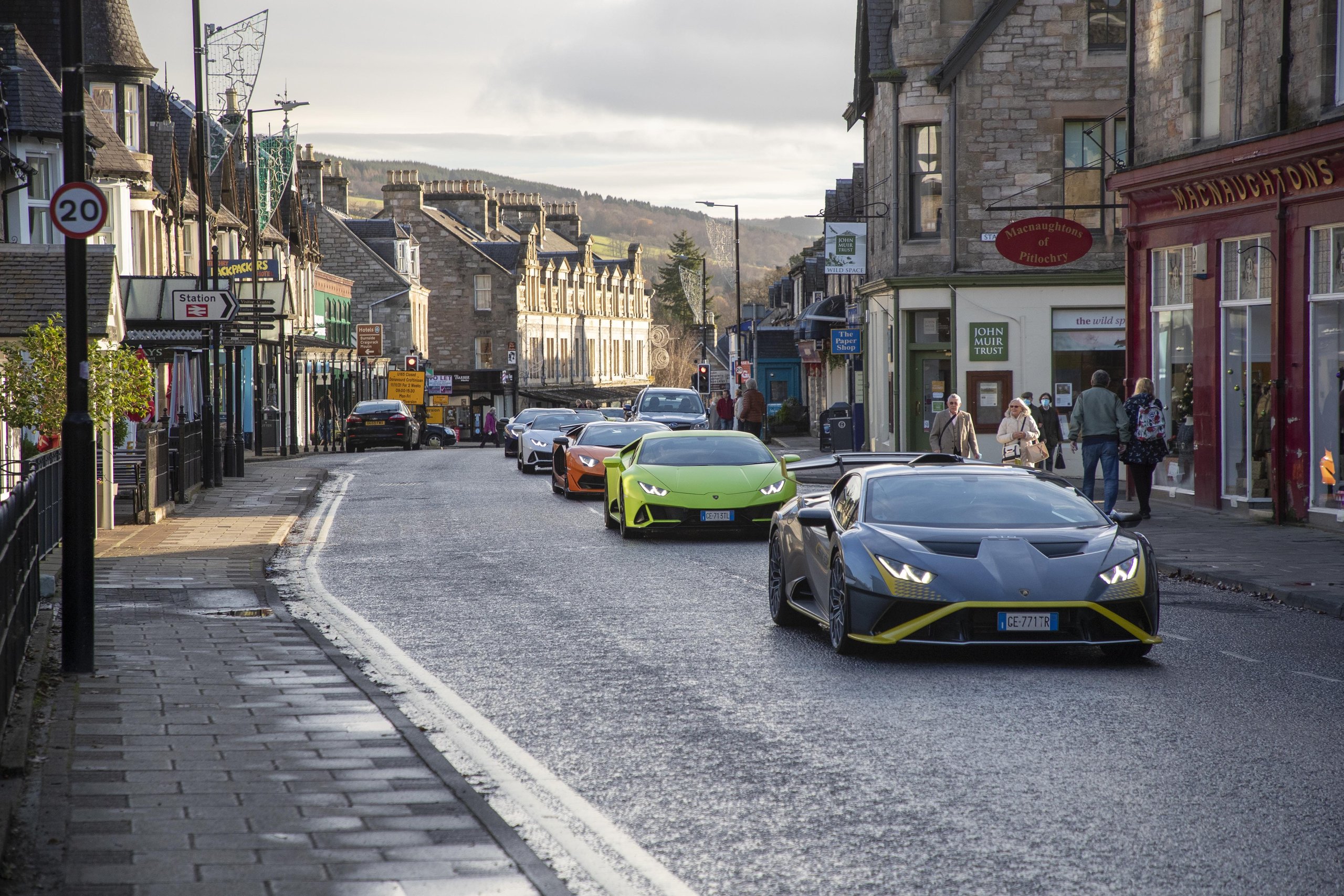 Lamborghini Sent Its Entire Lineup Into The Scottish Highlands, And The Real Destination Was The Stars 3 Colorful lamborghini supercars including a huracán sto and huracán evo drive through a narrow scottish village street as pedestrians watch