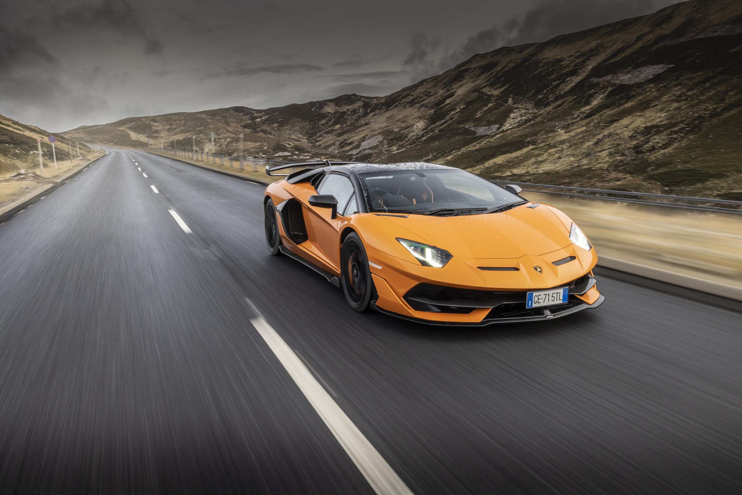 Lamborghini Sent Its Entire Lineup Into The Scottish Highlands, And The Real Destination Was The Stars 7 An orange aventador svj speeds down a wet, winding highland mountain road under dramatic cloudy skies