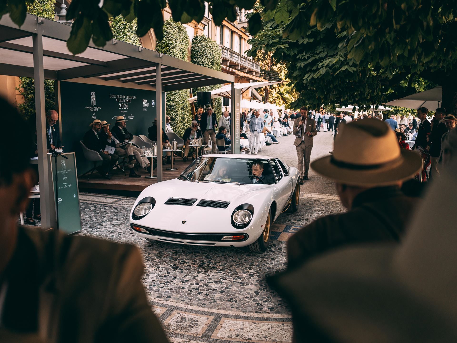 A white lamborghini miura sv driven on a cobblestone path at an elegant outdoor event