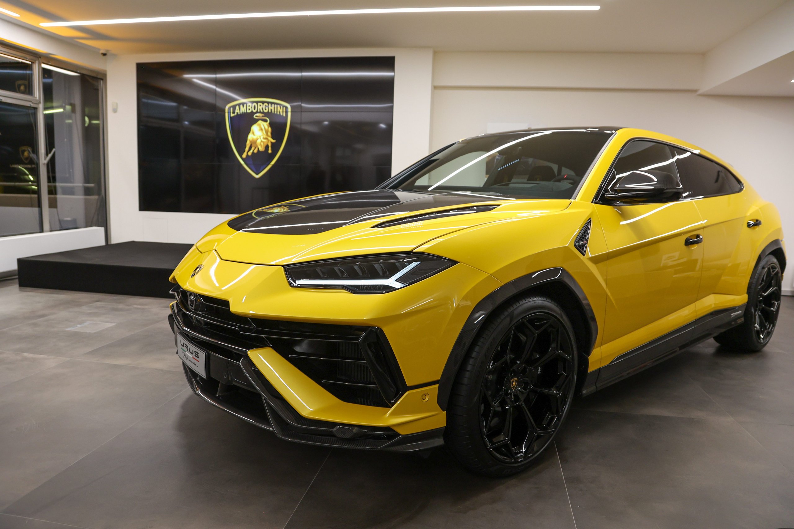 Lamborghini Prague Reopens With Urus Performante Premiere And A Glimpse Of What Comes Next 3 A vibrant yellow lamborghini urus performante with black accents displayed in the prague showroom, with a large lamborghini logo screen behind it