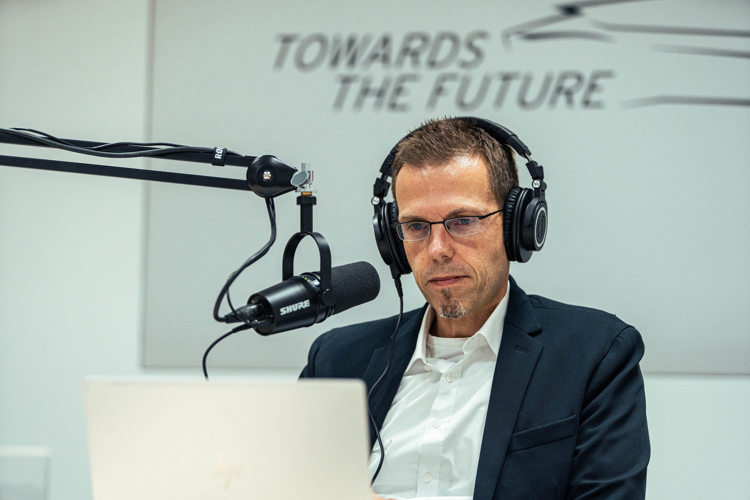 A man wearing headphones and glasses speaks into a shure microphone in a recording studio during the beyond podcast session