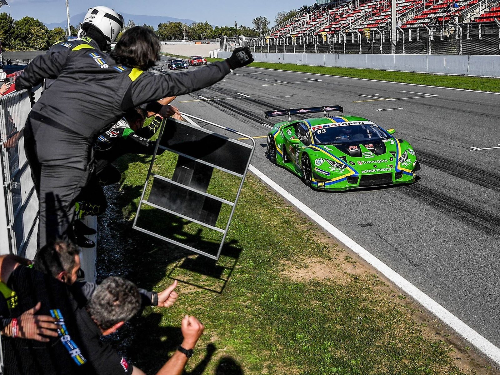 Green Lamborghini Huracán GT3 EVO racing past the pit wall as crew members cheer during a 2021 championship race