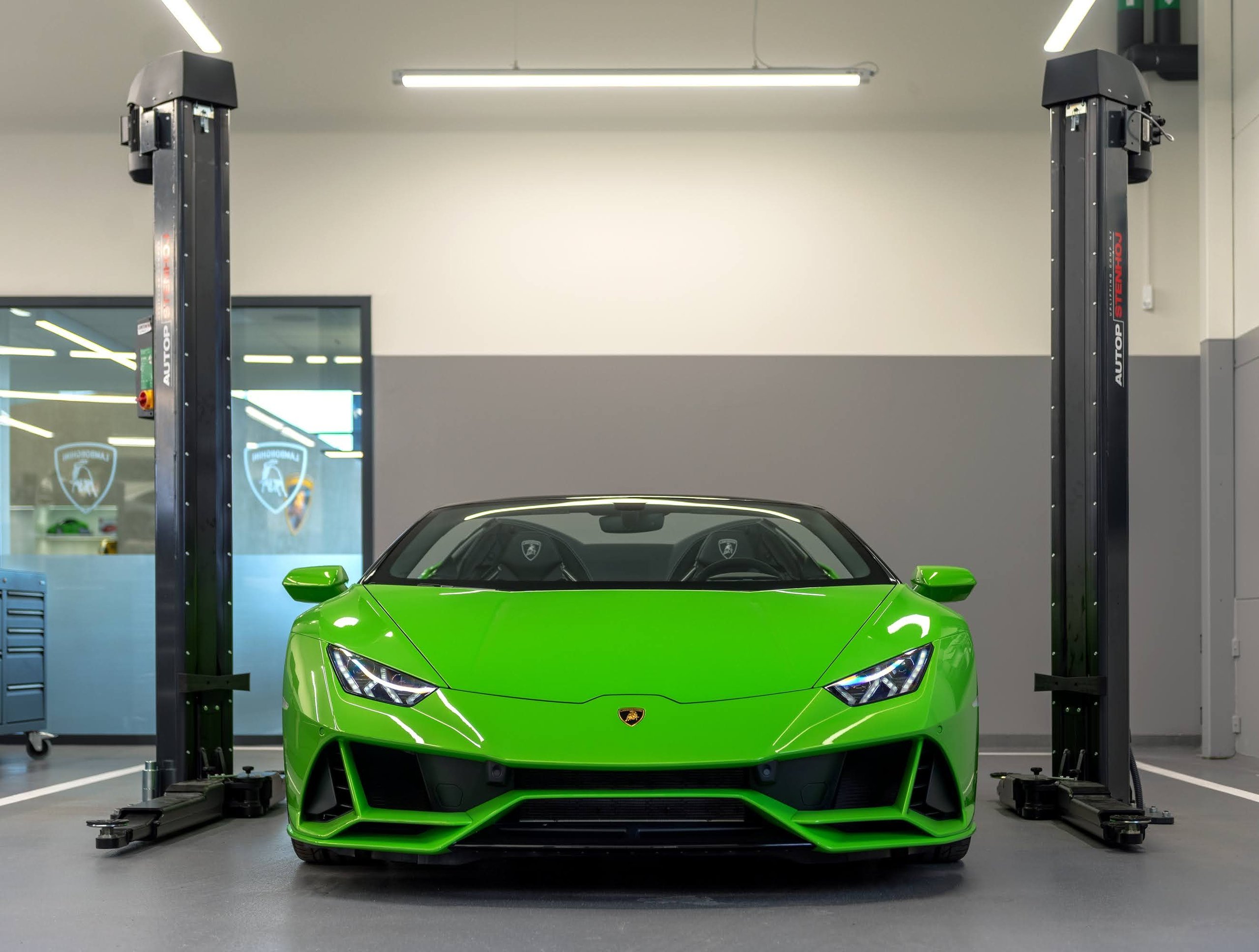 A green Lamborghini Huracán in the Stockholm dealership's clean service bay, positioned between two vehicle lifts