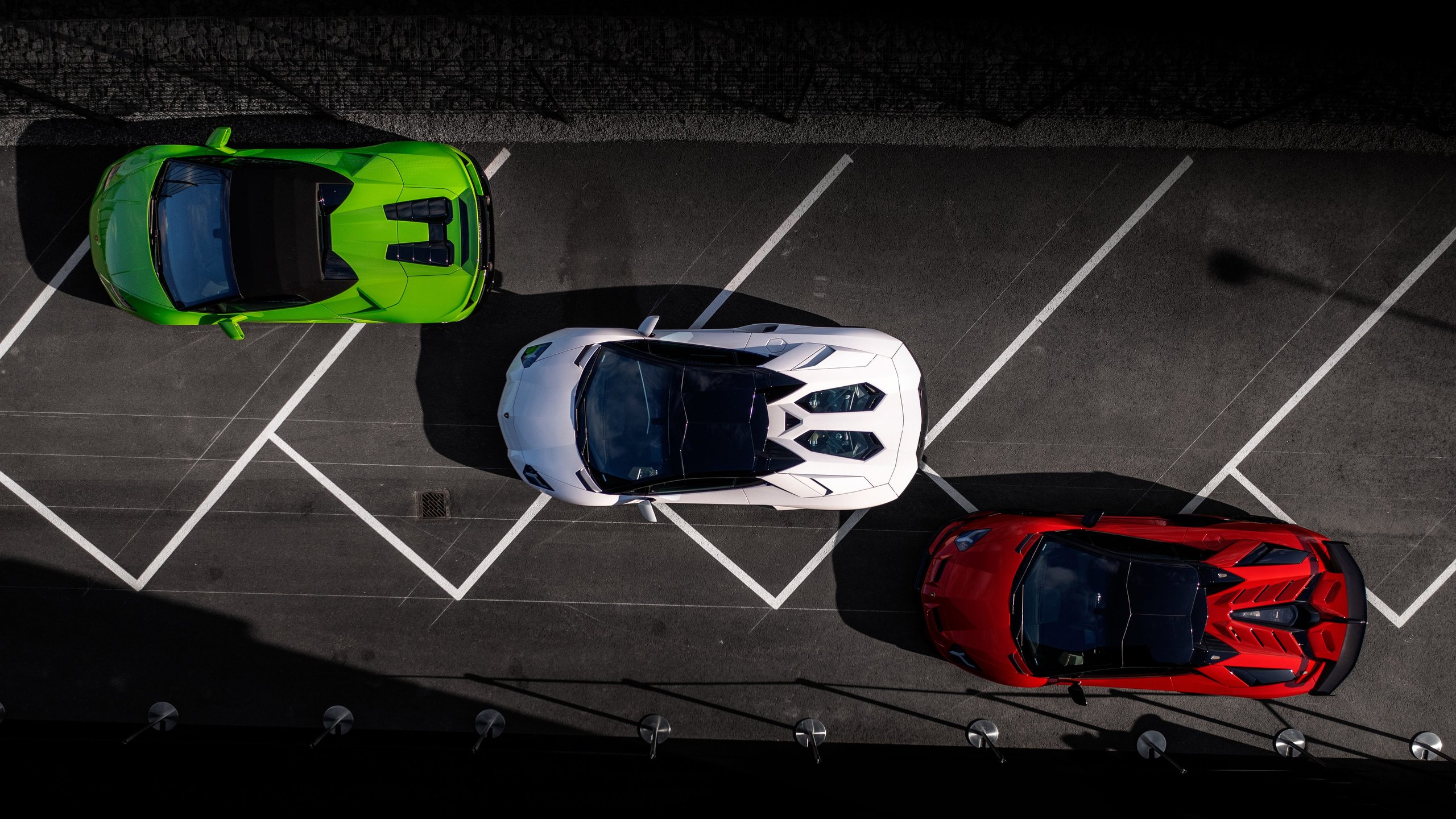 Aerial view of three Lamborghini supercars parked diagonally: a green Huracán, white Aventador, and red Aventador SVJ
