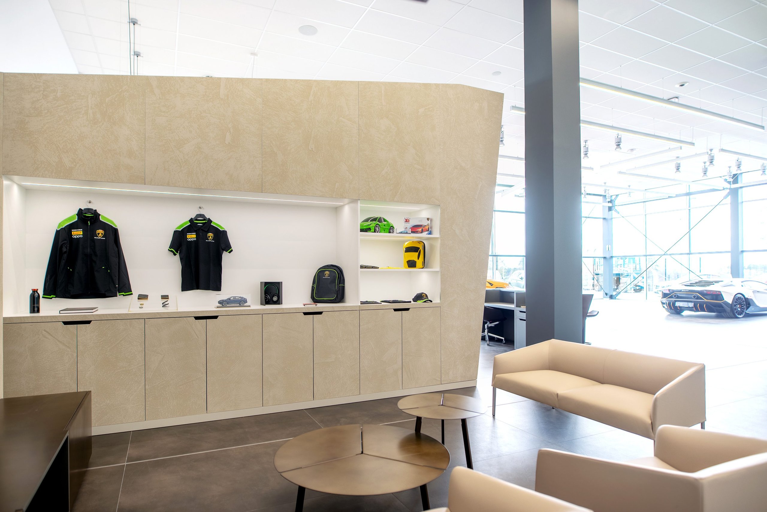 Lamborghini Stockholm lounge area with branded merchandise display and a white Aventador visible through glass partitions