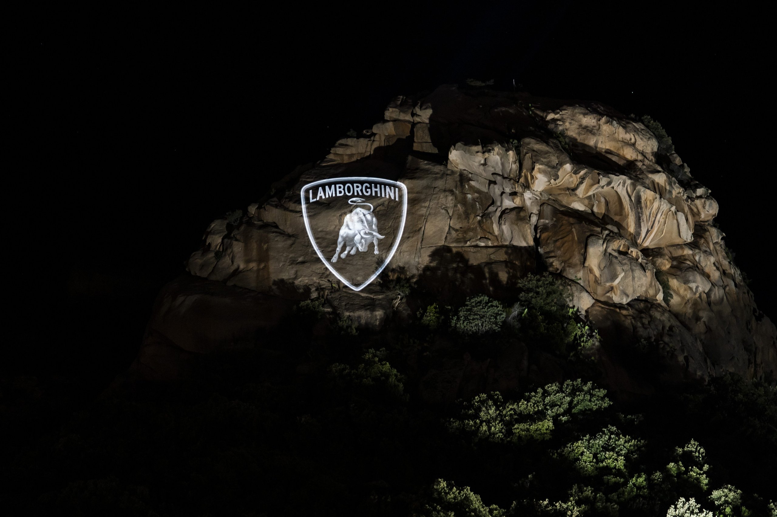 Lamborghini shield logo projected onto a rocky Sardinian hillside at night