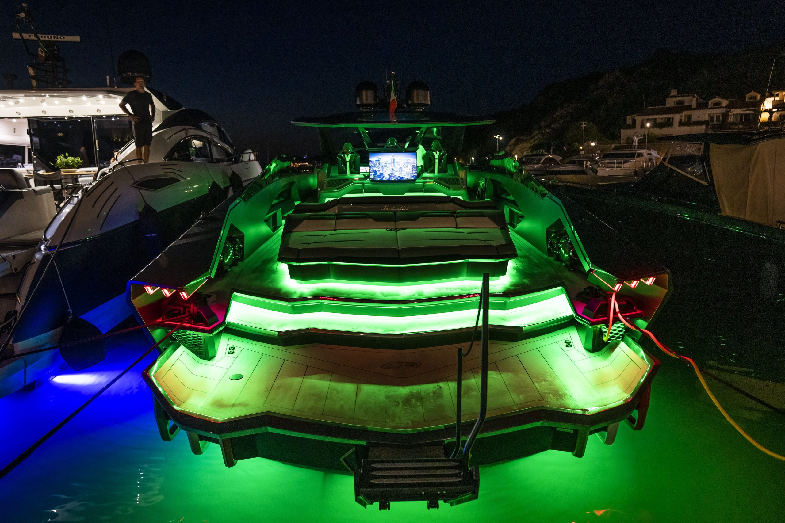 Tecnomar for Lamborghini 63 yacht docked at night, illuminated with green and blue underwater lights showing its angular rear design