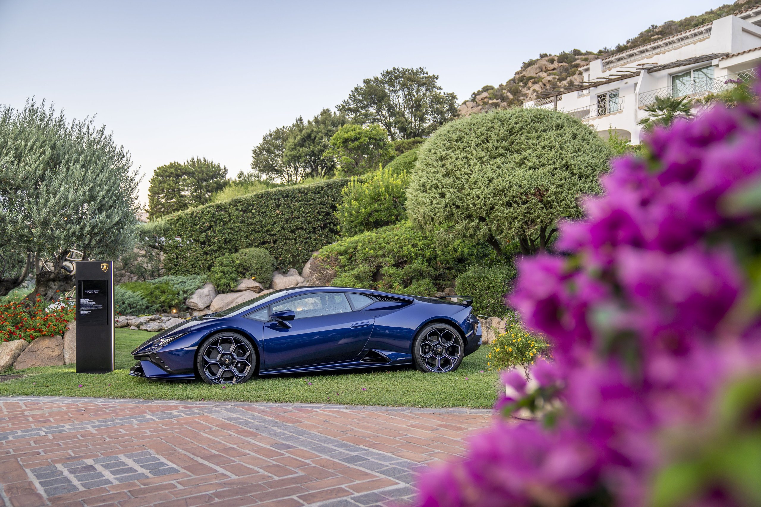 Blue Lamborghini Huracán Tecnica in full side profile on a grassy lawn at an outdoor event in Sardinia