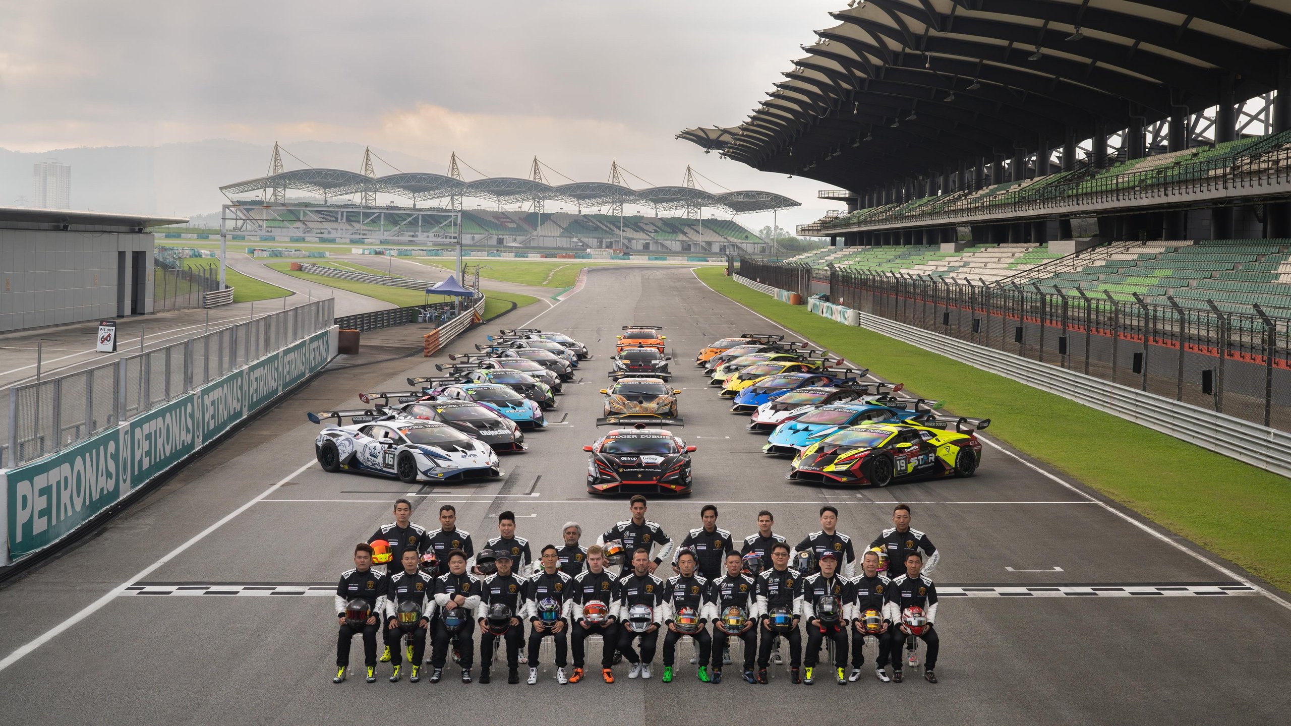 Lamborghini Super Trofeo'S 2024 Calendar Puts Customer Racing On The World'S Biggest Stages, Starting With Le Mans 9 Group of race car drivers in racing suits posing in front of a large array of lamborghini huracán super trofeo evo2 cars on a racetrack