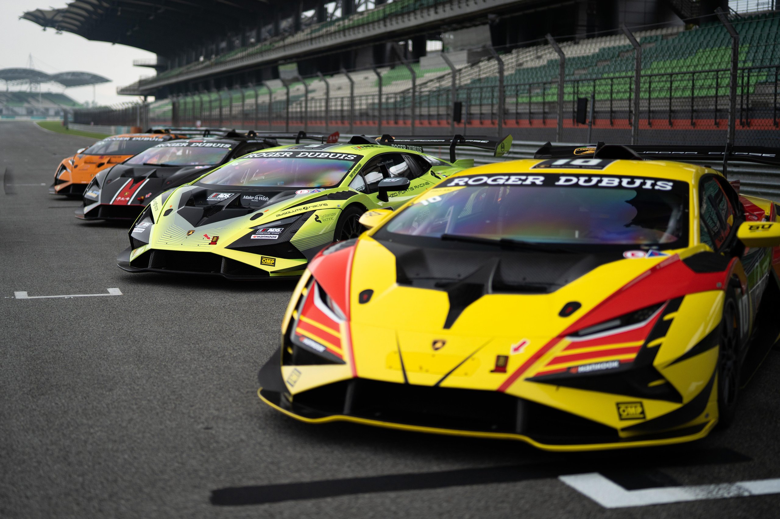 Lamborghini Super Trofeo'S 2024 Calendar Puts Customer Racing On The World'S Biggest Stages, Starting With Le Mans 5 Line of lamborghini huracán super trofeo evo2 race cars with a yellow and red car prominent in the foreground, parked on a racetrack
