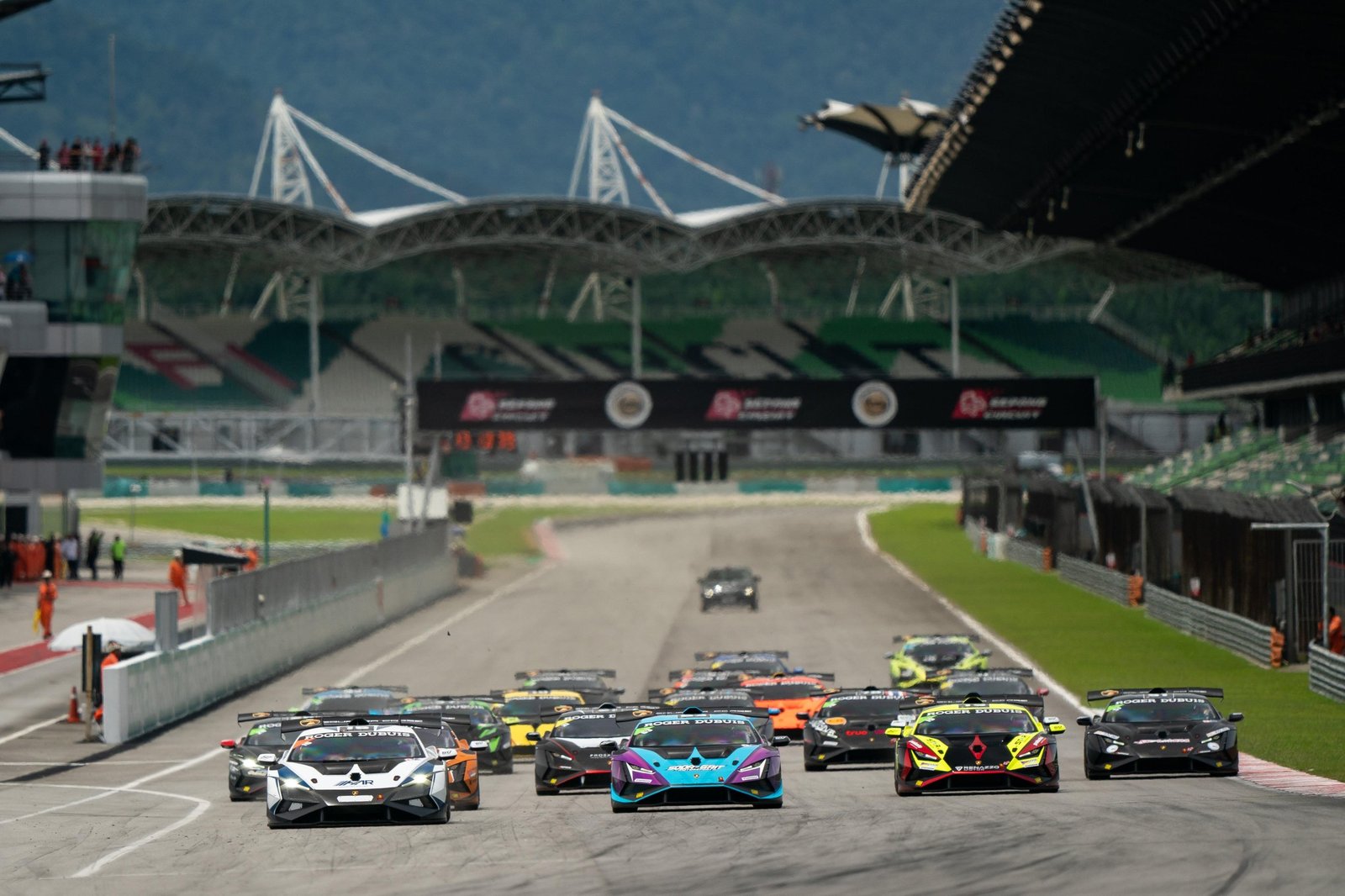 Pack of Lamborghini Huracán Super Trofeo EVO2 race cars launching from the starting grid with grandstands and mountains in the background