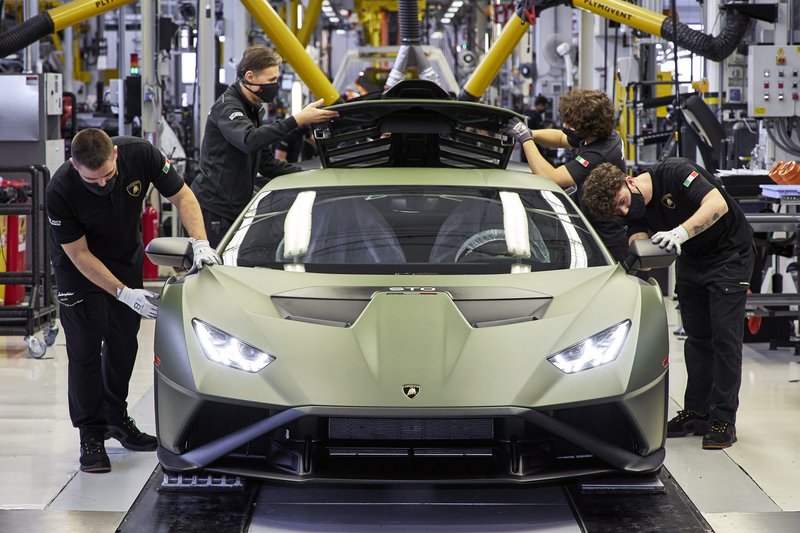 Four Lamborghini technicians in masks and gloves inspect a matte green Huracán STO on the Sant'Agata Bolognese factory floor