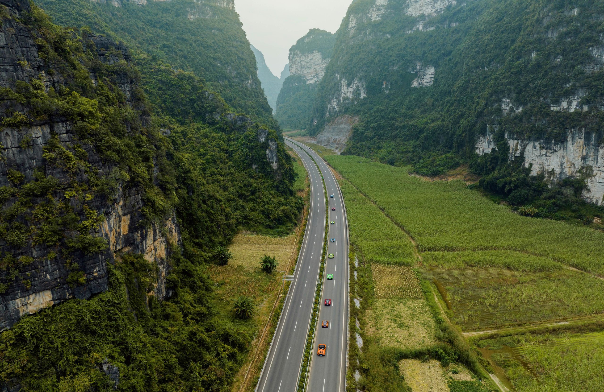 Lamborghini'S Own Employees Voted It A Sustainability Champion, And That Matters More Than The Trophy 7 Aerial view of a convoy of colorful lamborghini vehicles driving along a winding highway through a lush green valley surrounded by mountains