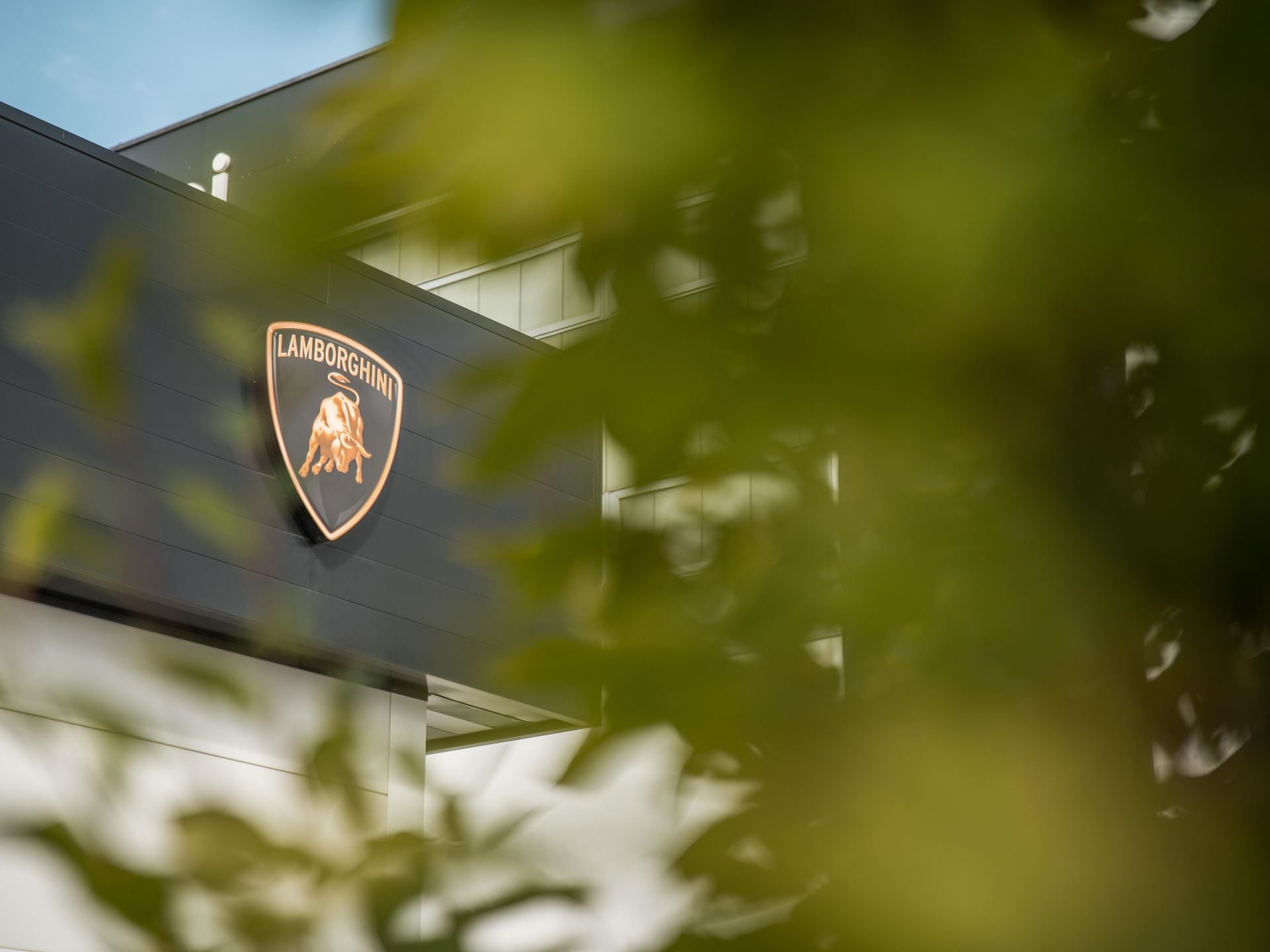 Lamborghini'S Own Employees Voted It A Sustainability Champion, And That Matters More Than The Trophy 3 Lamborghini shield logo on a dark building facade partially obscured by green foliage