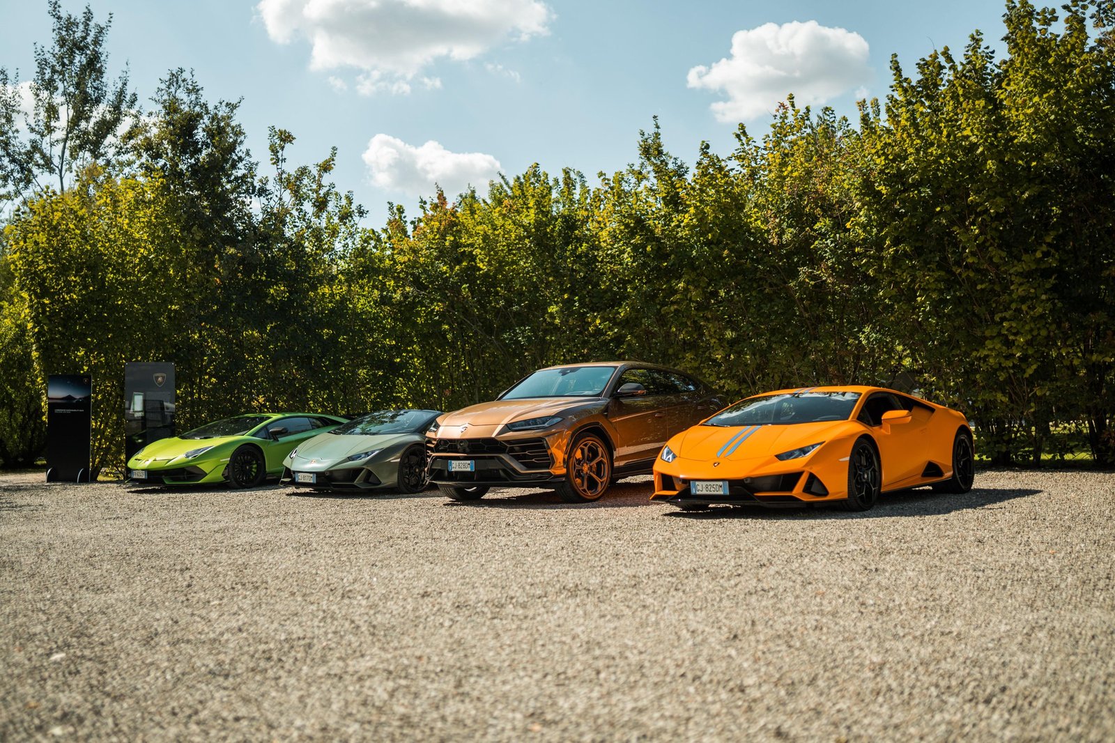 Four Lamborghini vehicles including Huracán and Urus models parked on gravel with lush green foliage behind them