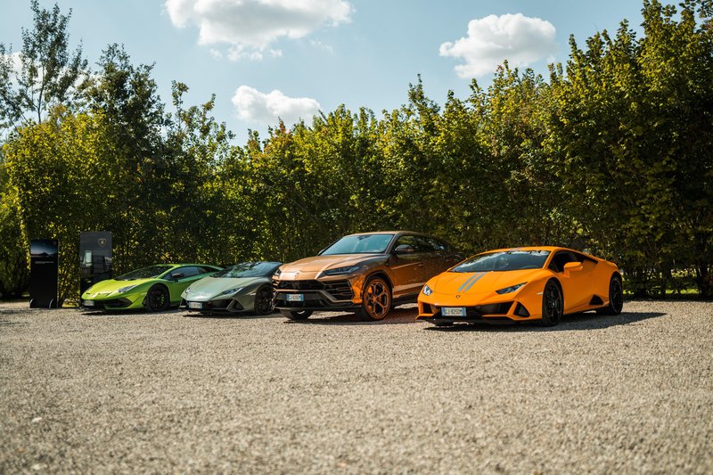 Four Lamborghini vehicles including Huracán and Urus models parked on gravel with lush green foliage behind them