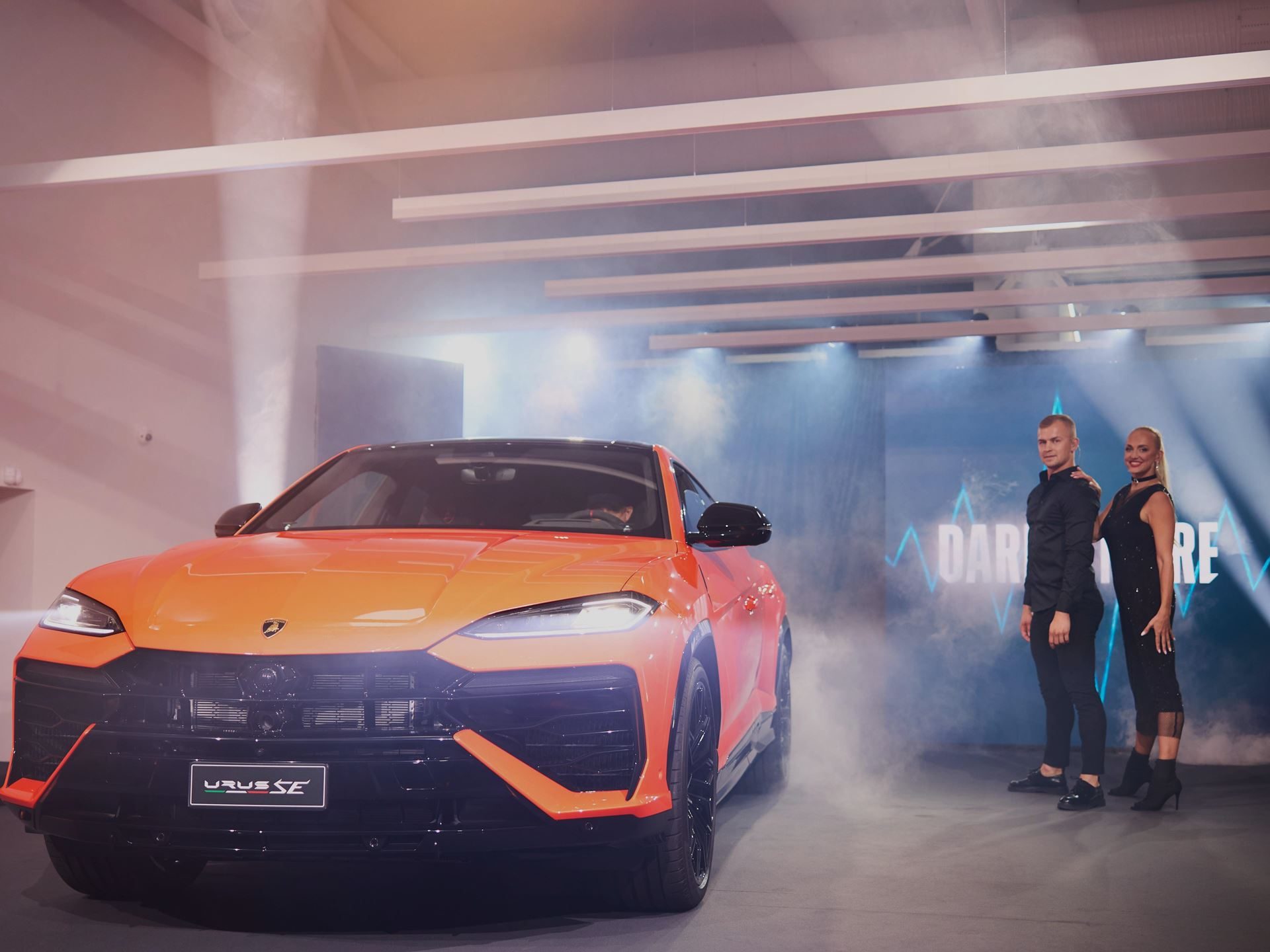 Lamborghini Tallinn'S New Showroom Pairs A Choir, A Diablo, And The Urus Se To Sell Its Hybrid Future 3 Orange lamborghini urus se unveiled on stage with dramatic lighting and smoke effects at the tallinn showroom opening