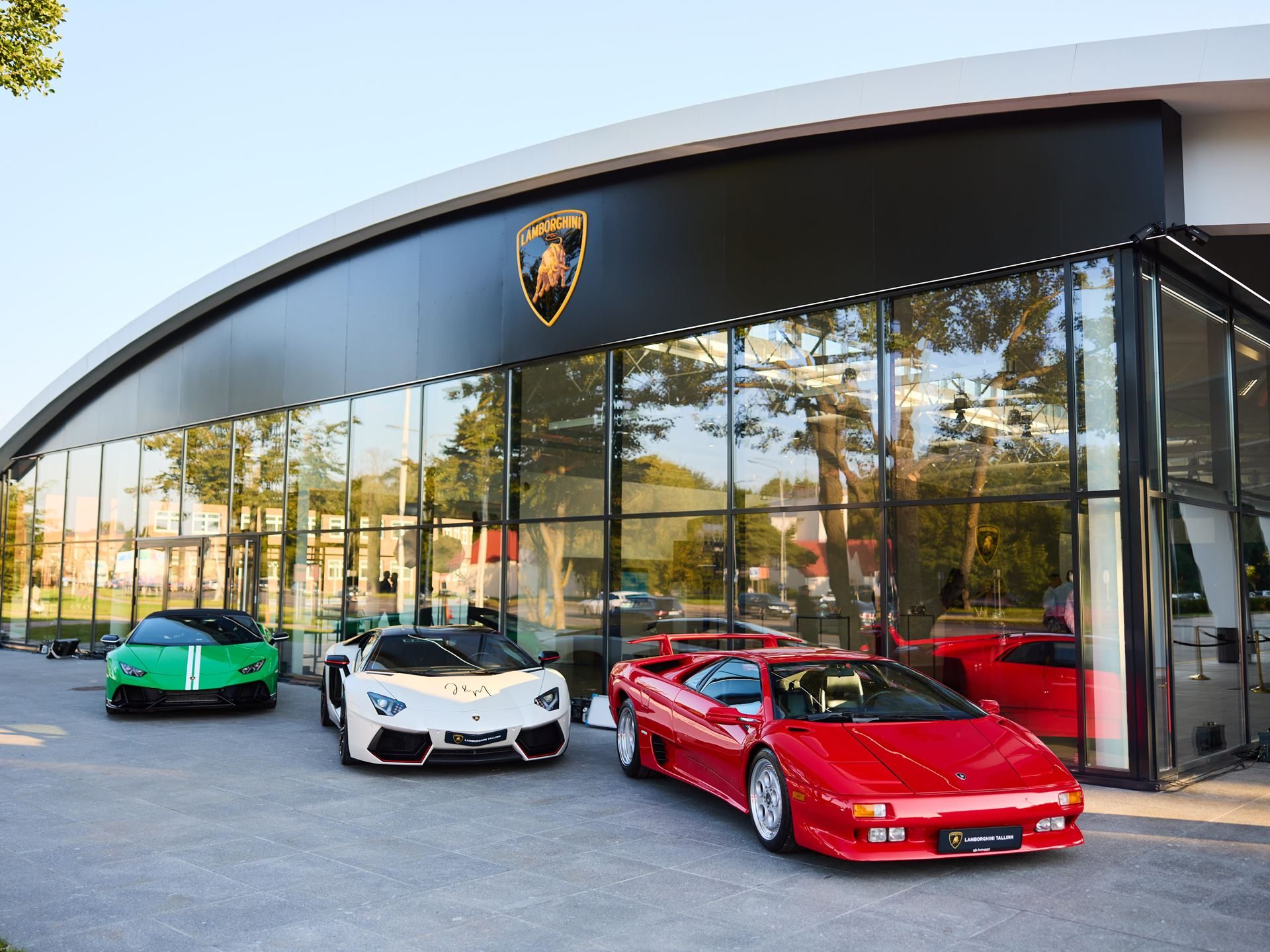 Lamborghini Tallinn'S New Showroom Pairs A Choir, A Diablo, And The Urus Se To Sell Its Hybrid Future 5 Daytime exterior of lamborghini tallinn showroom with a green huracan, white huracan, and red diablo parked outside