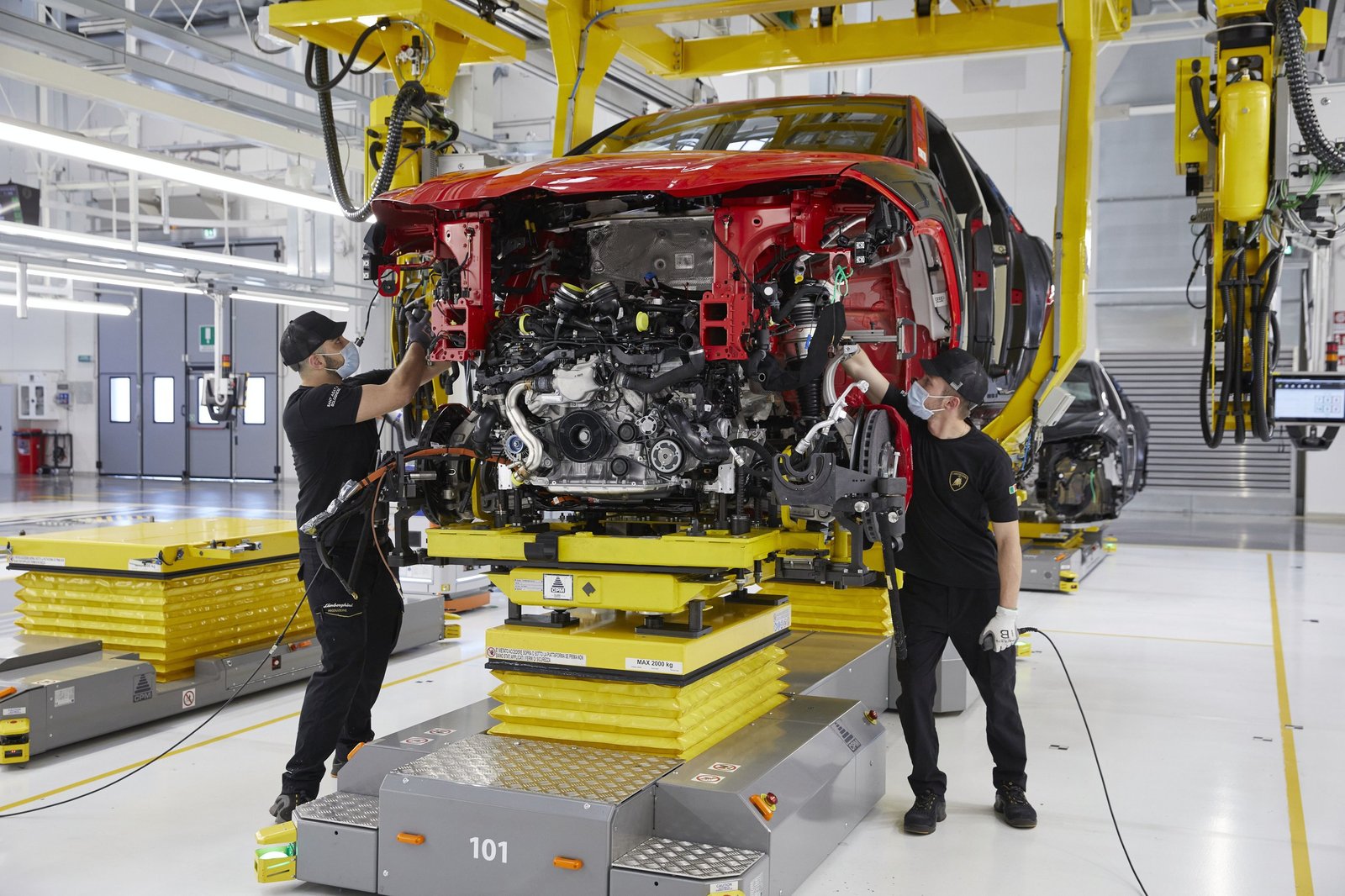 Two Lamborghini technicians assembling the front section of a red Urus chassis on the factory line