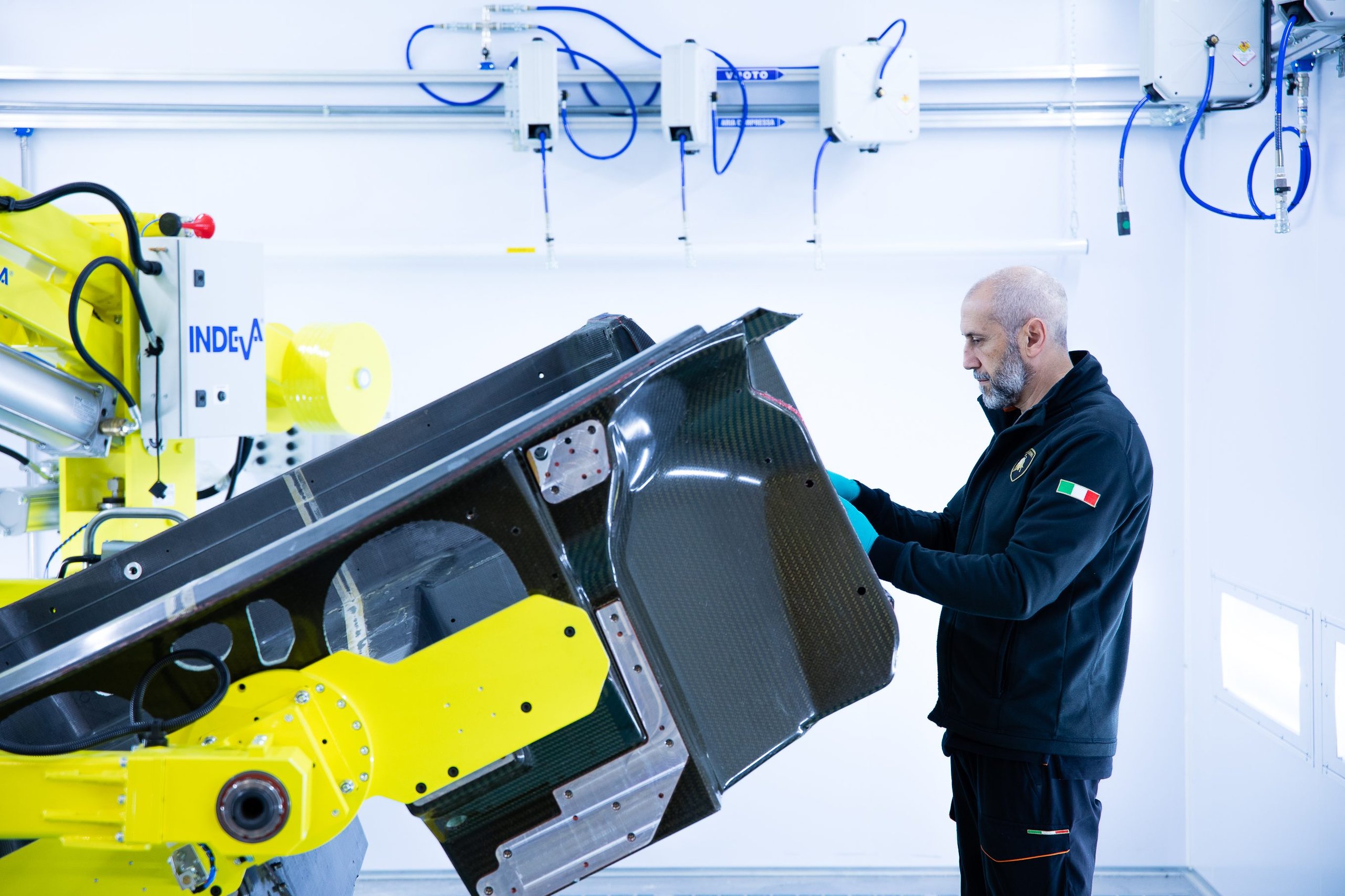 Italy'S Most Desirable Automotive Employer Builds Lamborghinis, And That Matters More Than You Think 13 Lamborghini worker inspecting a large dark composite component on a yellow robotic arm in the factory