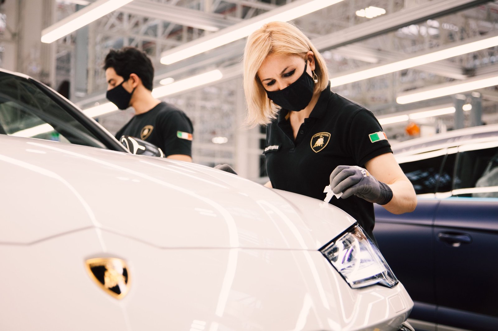 A female Lamborghini employee performs a final quality inspection on the front of a white Lamborghini Urus at the Sant'Agata Bolognese factory