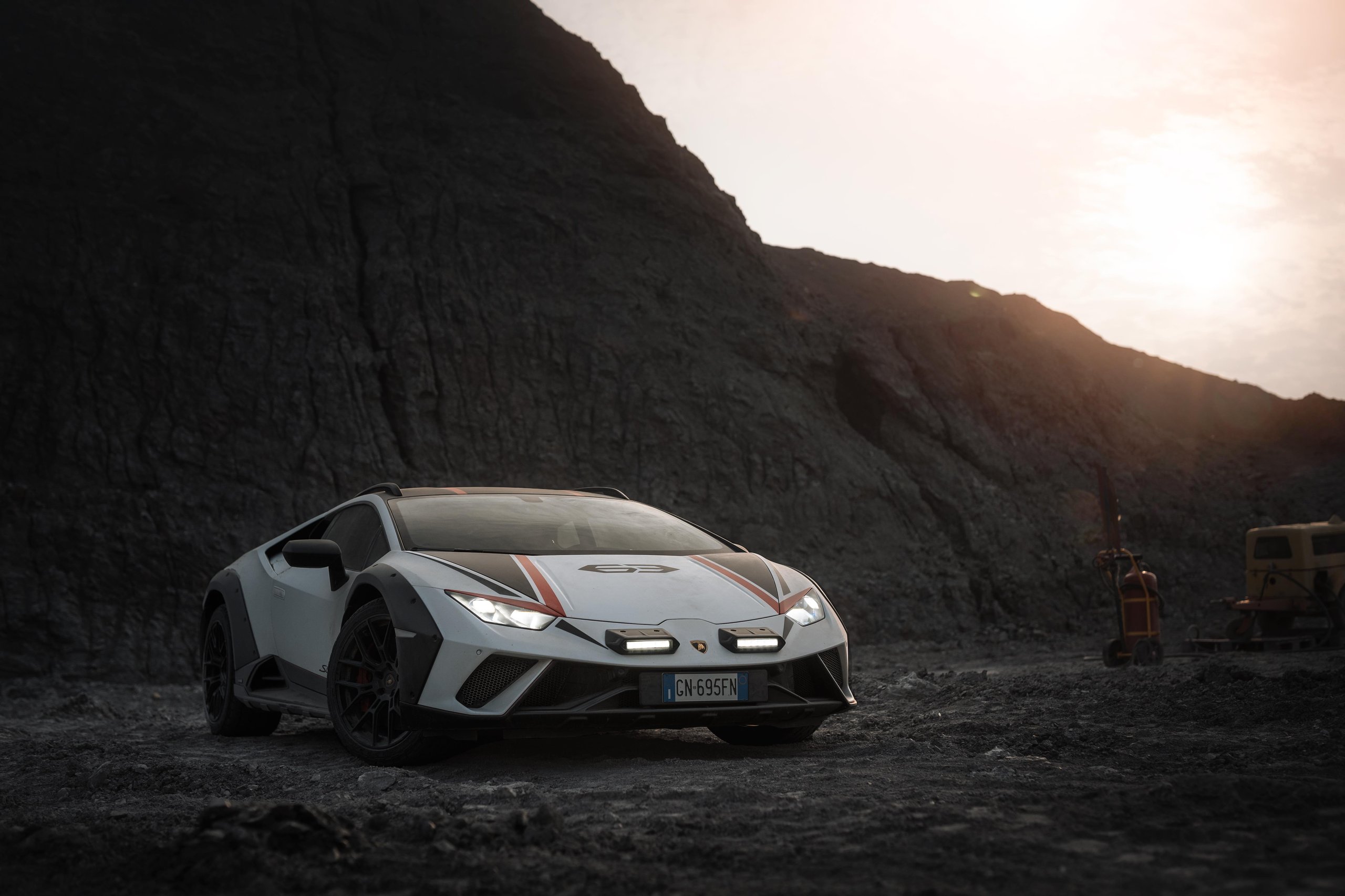 White lamborghini huracán sterrato with red and black racing stripes parked on rocky terrain at sunset