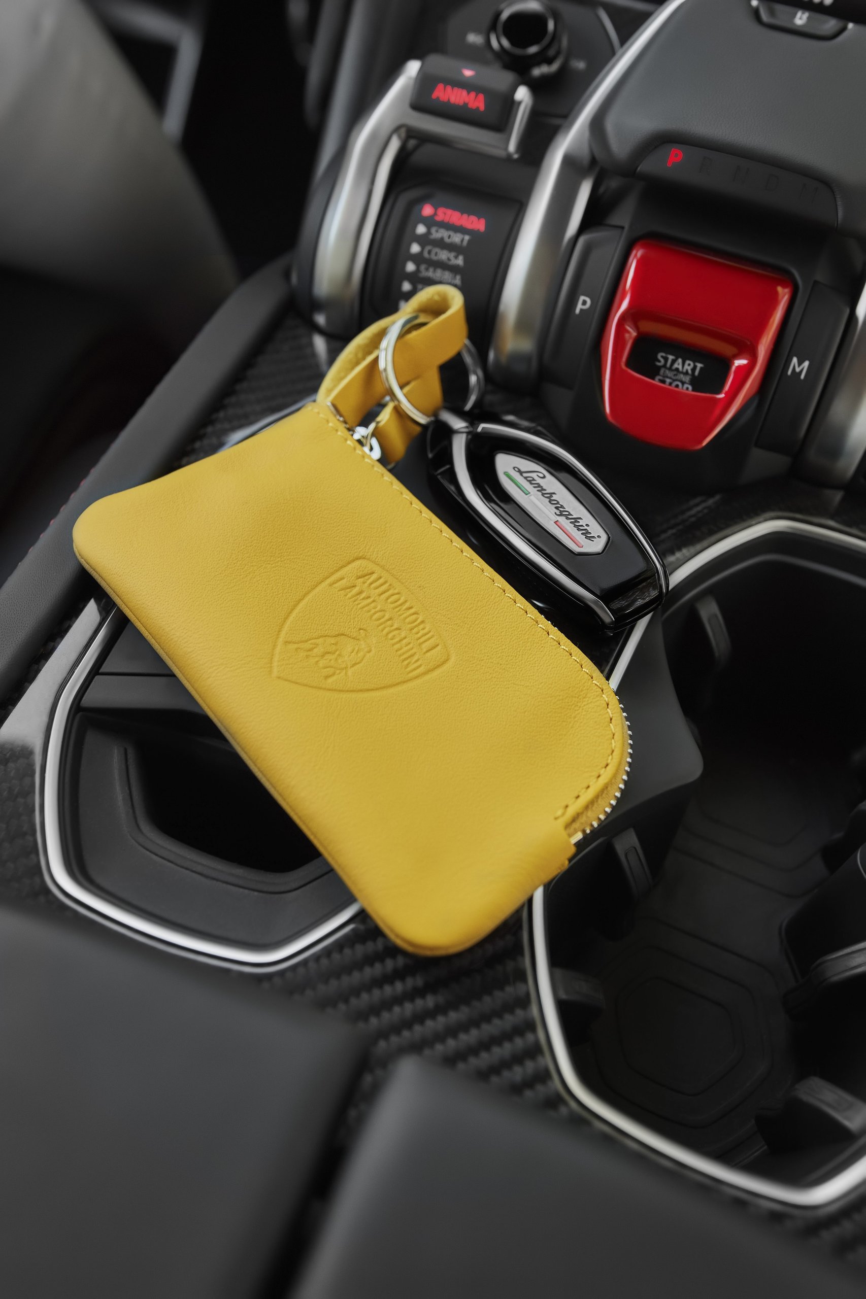 Lamborghini'S Upcycled Leather Project Turns Supercar Factory Scraps Into Covetable Accessories 9 Yellow leather key case with lamborghini logo and car key resting on carbon fiber console of a lamborghini urus near the start/stop button