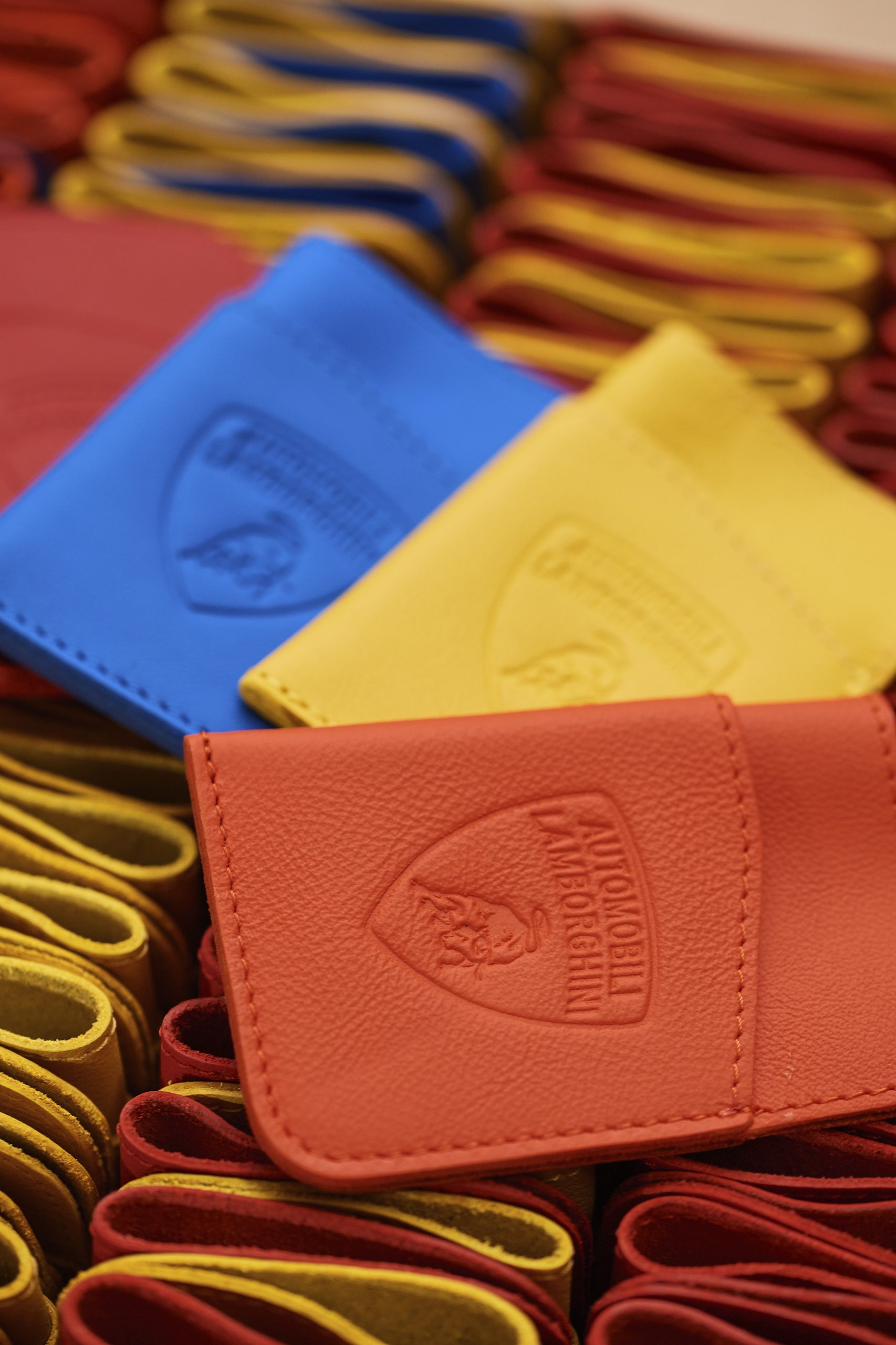 Lamborghini'S Upcycled Leather Project Turns Supercar Factory Scraps Into Covetable Accessories 11 Three colorful leather card holders in red, yellow, and blue with embossed lamborghini logos resting on folded leather pieces