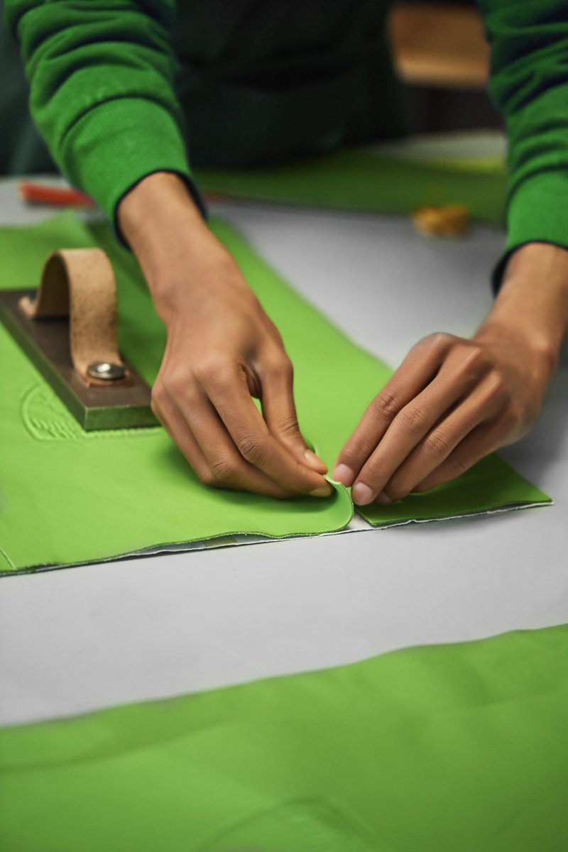 Artisan hands carefully folding green leather at Cartiera's workshop with a leather press visible in the background