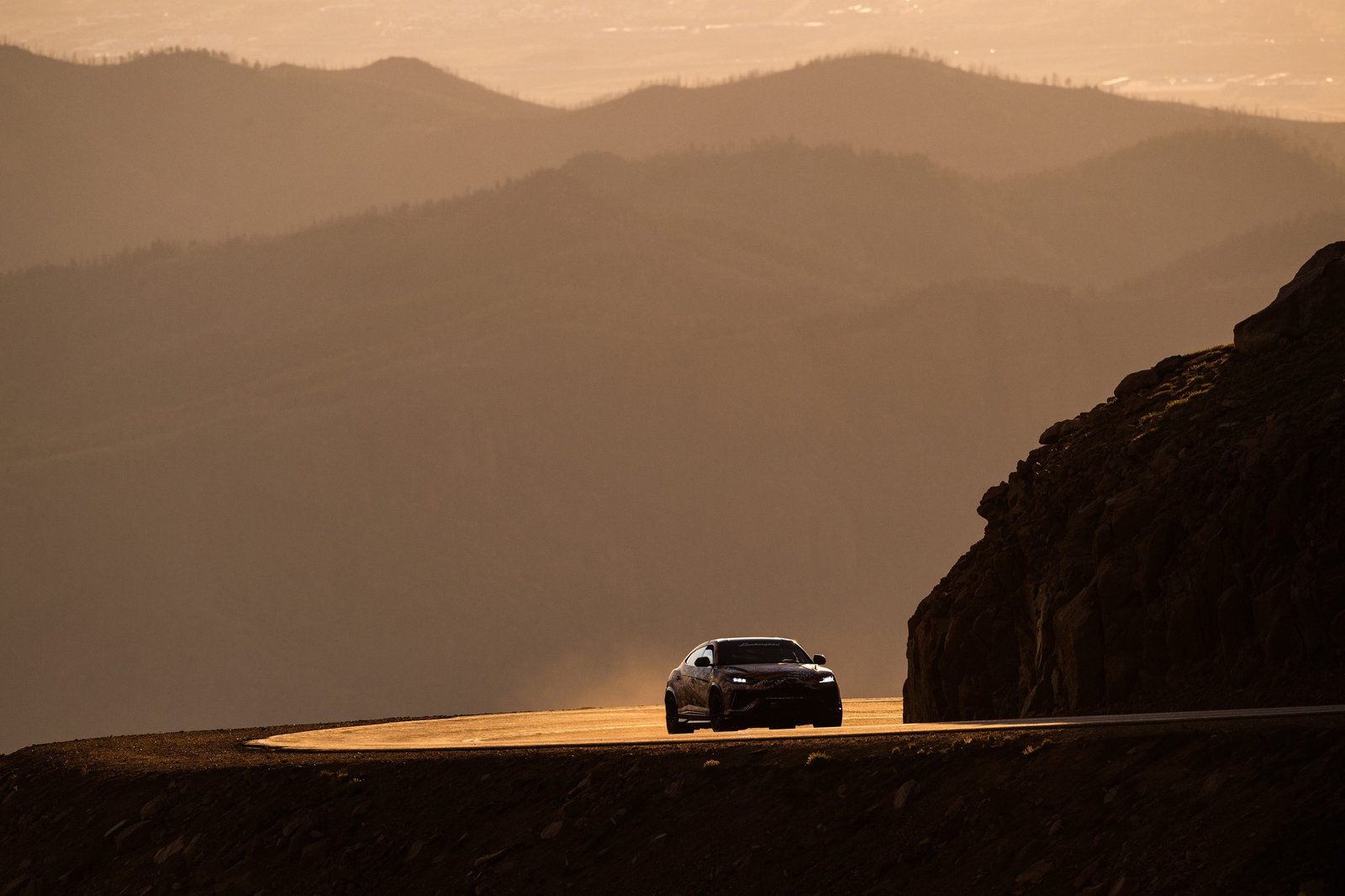 Lamborghini Urus driving on a winding mountain road at Pikes Peak during sunset