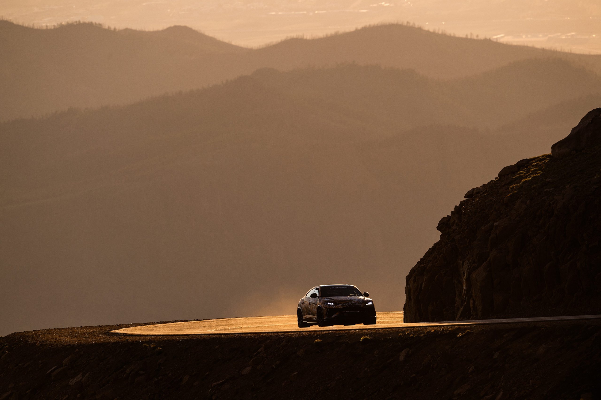 Lamborghini urus driving on a winding mountain road at pikes peak during sunset