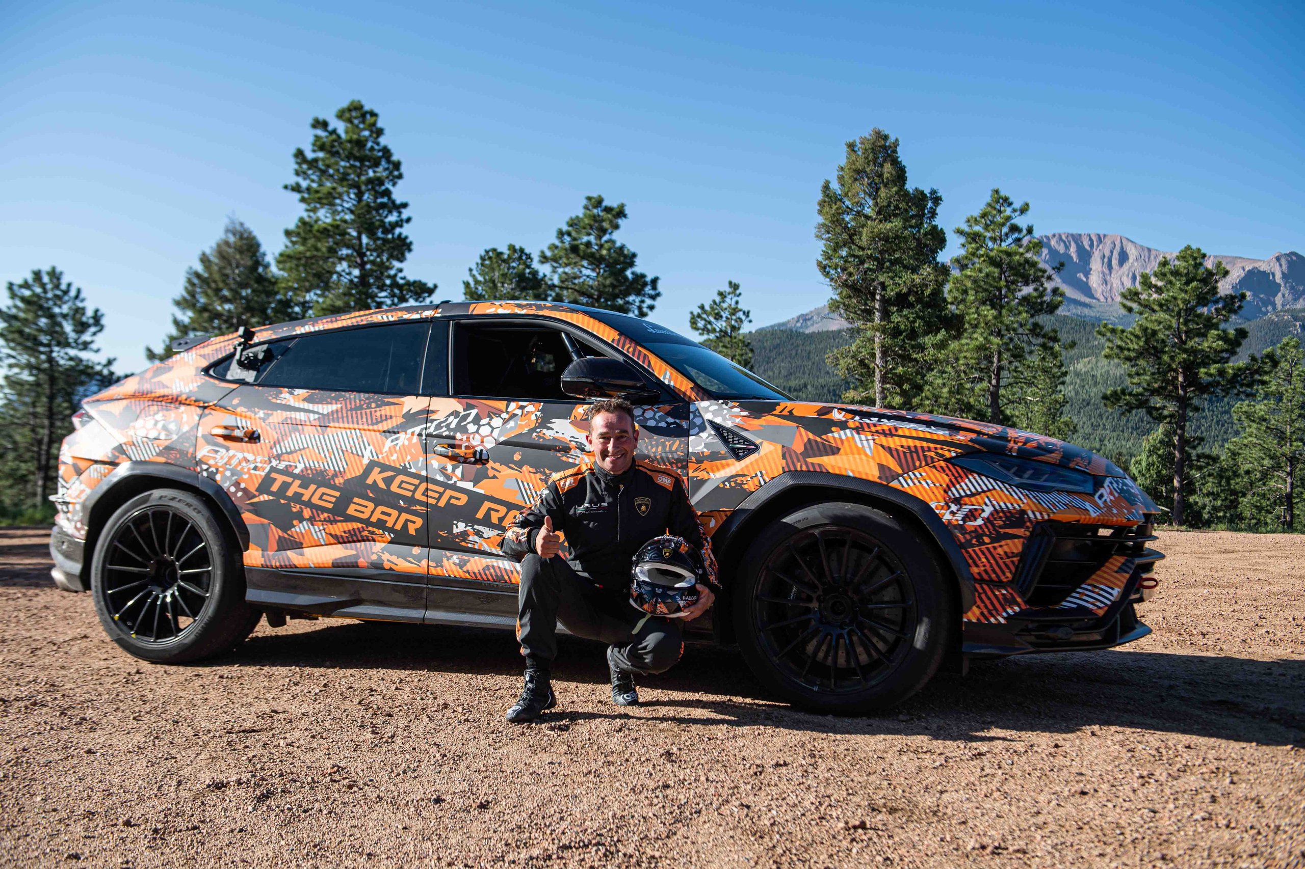 A Camouflaged Urus Just Demolished The Pikes Peak Suv Record By 17 Seconds 7 Driver simone faggioli kneeling beside the camouflaged lamborghini urus performante holding his helmet at pikes peak