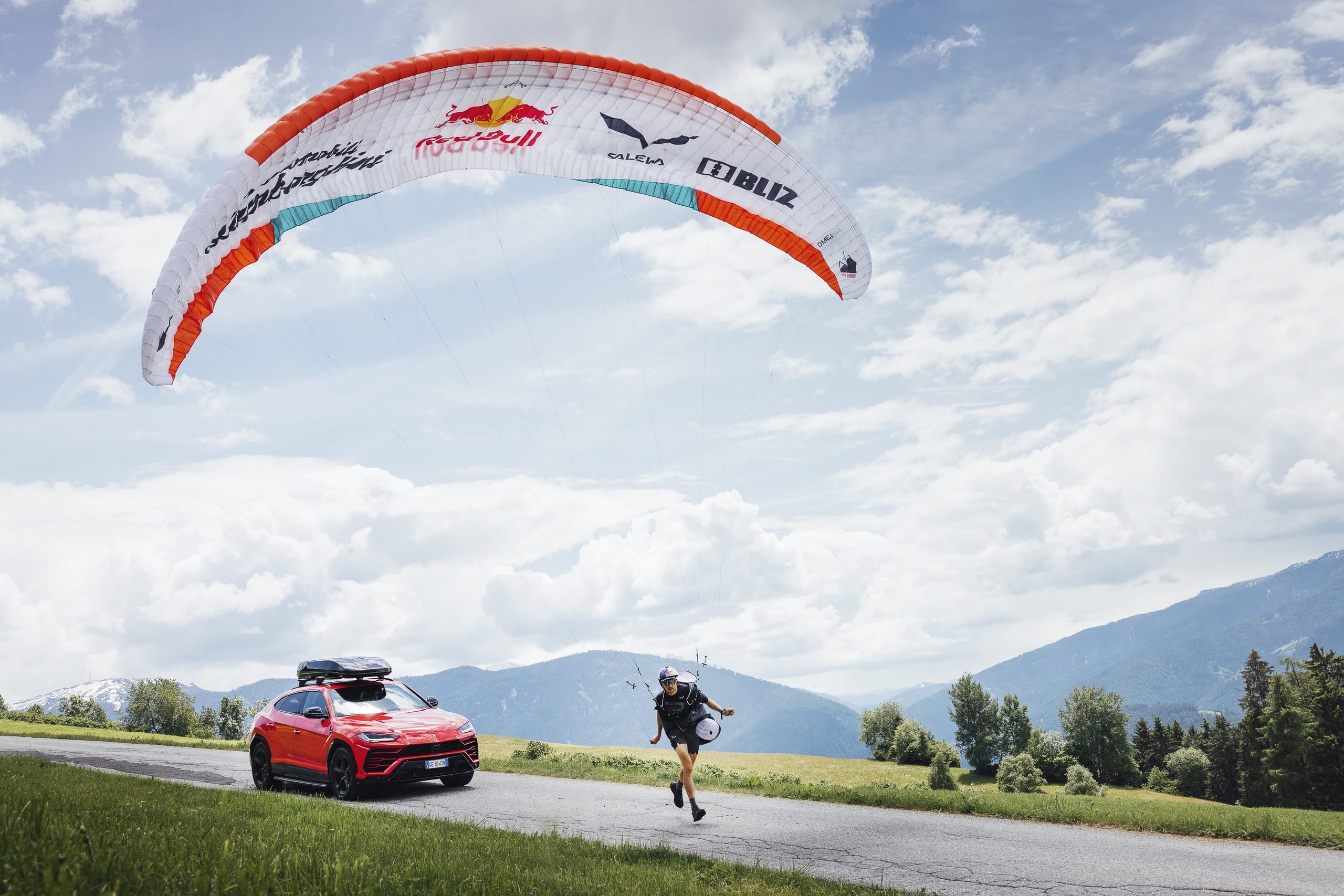 How The Lamborghini Urus Became A Support Vehicle For One Of The World'S Toughest Races 3 Red lamborghini urus with roof box parked on a winding mountain road as aaron durogati launches a lamborghini-branded paraglider
