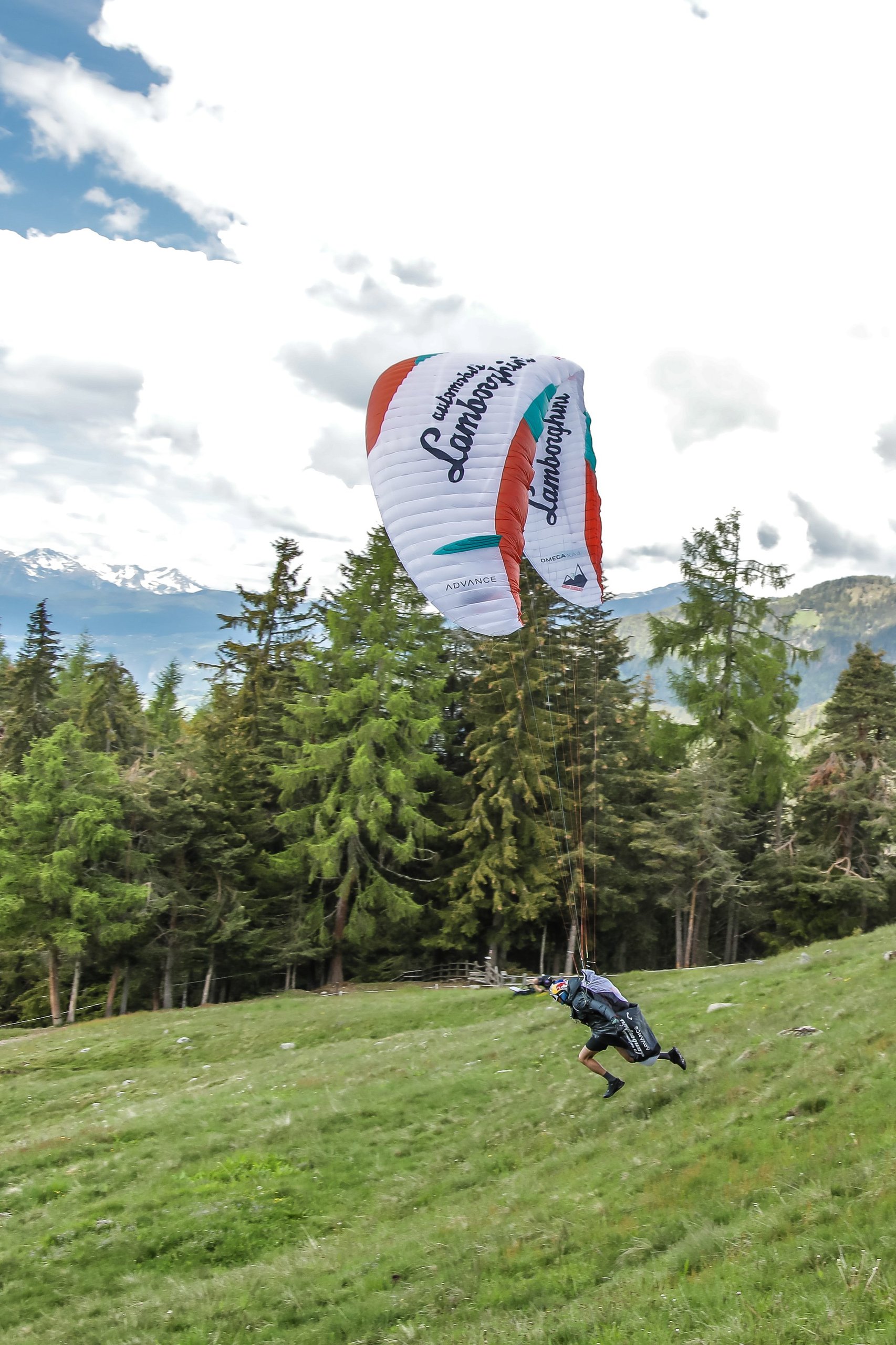 How The Lamborghini Urus Became A Support Vehicle For One Of The World'S Toughest Races 5 Aaron durogati launching a lamborghini-branded paraglider from a grassy alpine slope with pine trees and mountains behind