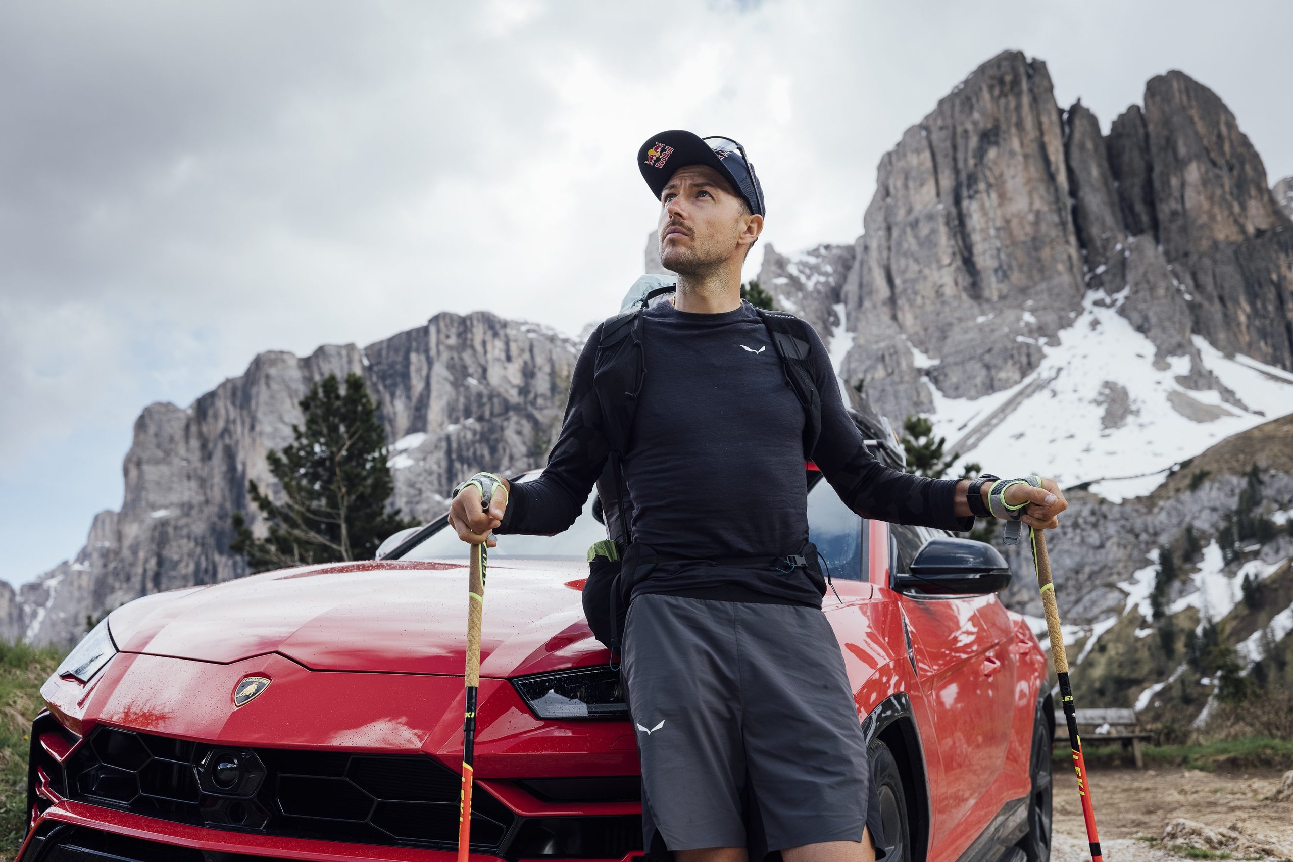 How The Lamborghini Urus Became A Support Vehicle For One Of The World'S Toughest Races 9 Aaron durogati holding trekking poles and leaning against a red lamborghini urus with majestic snow-capped mountains in the background