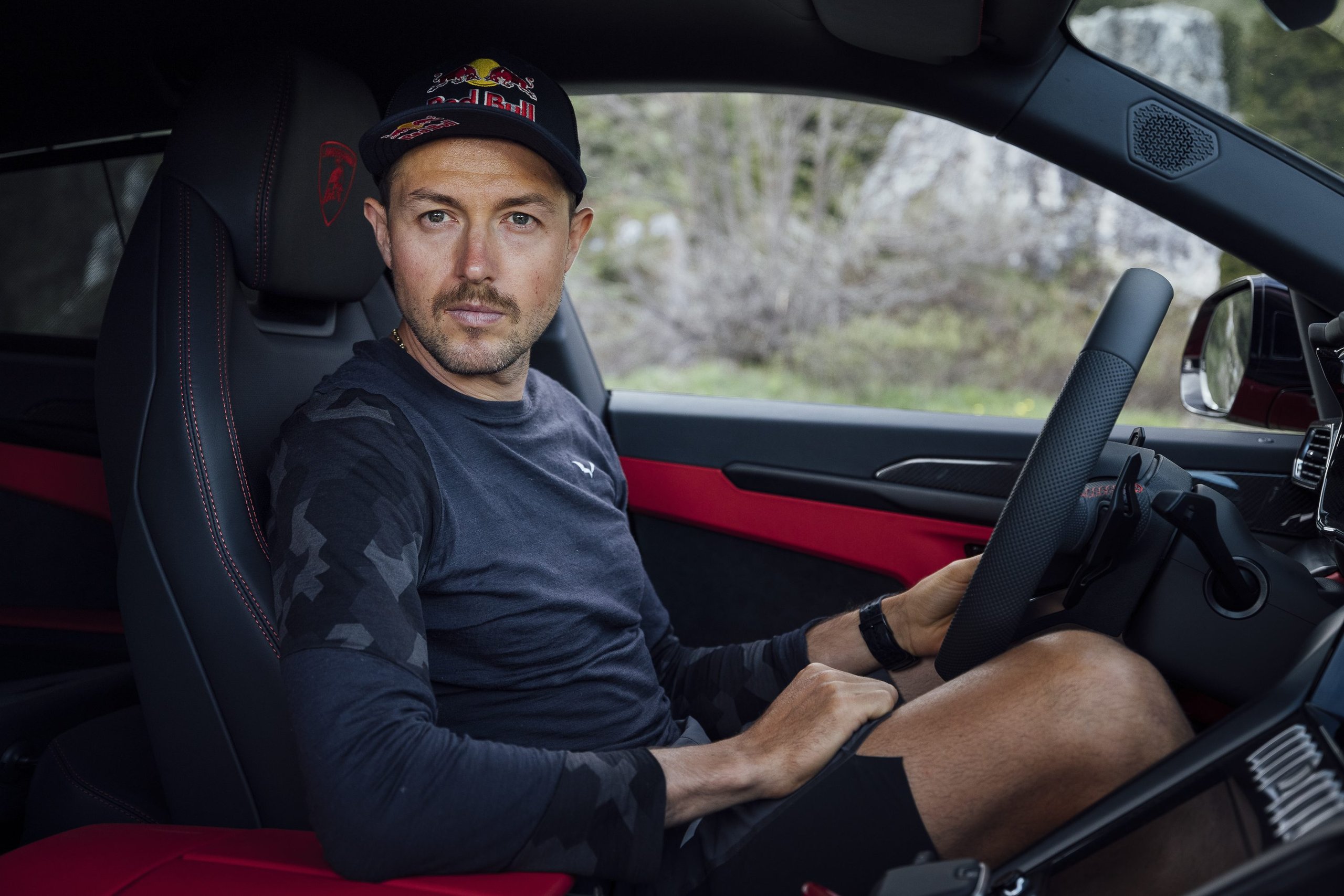 How The Lamborghini Urus Became A Support Vehicle For One Of The World'S Toughest Races 7 Aaron durogati wearing a red bull cap seated in the lamborghini urus interior with red-accented hexagonal stitching and flat-bottom steering wheel
