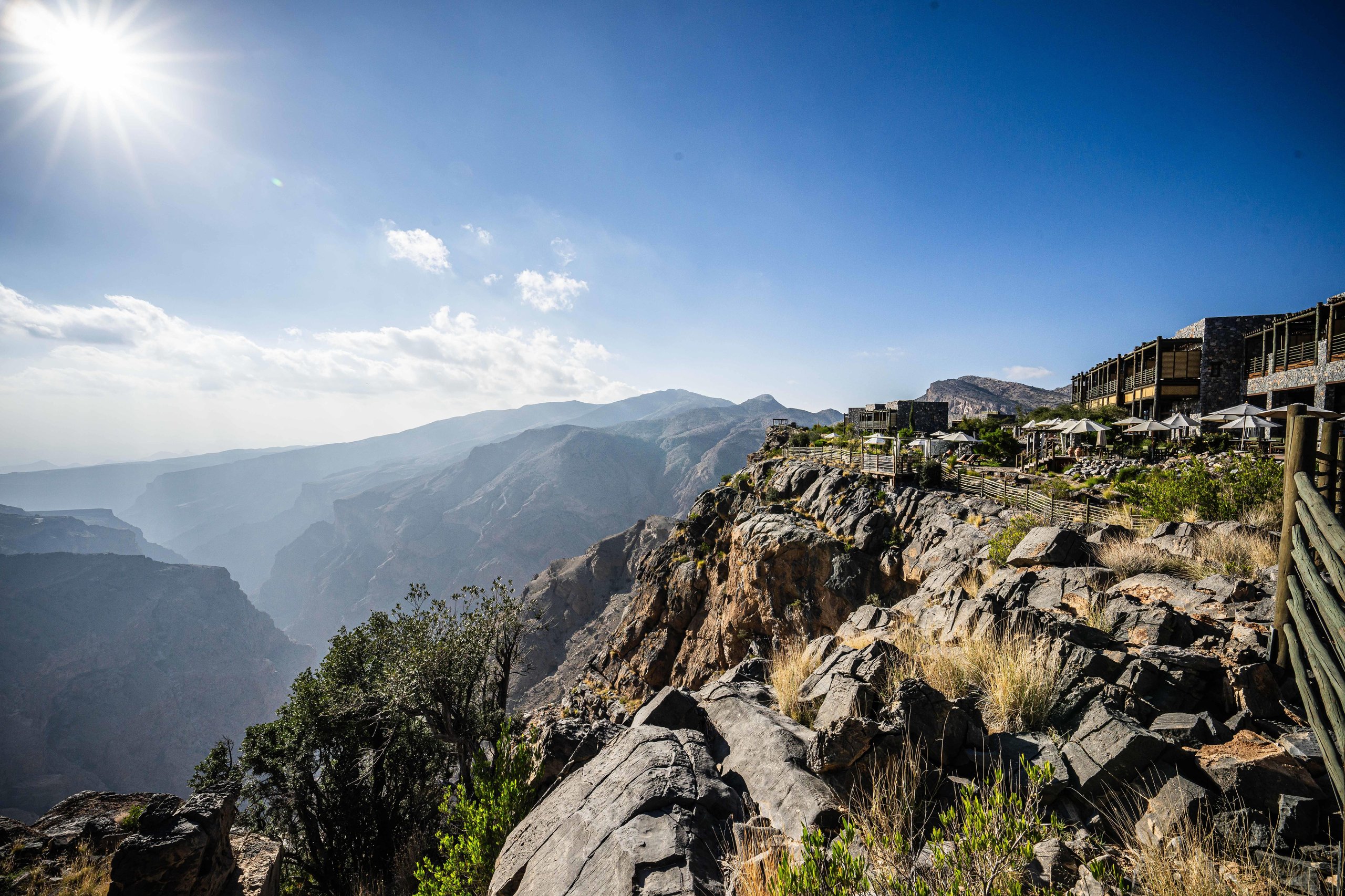 Panoramic view of alila jabal akhdar resort perched on a cliff edge overlooking a vast mountain canyon