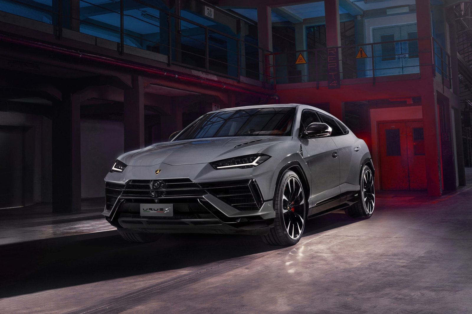Front three-quarter view of the Lamborghini Urus S in matte grey with Y-shaped DRLs, aggressive front fascia, and red brake calipers visible