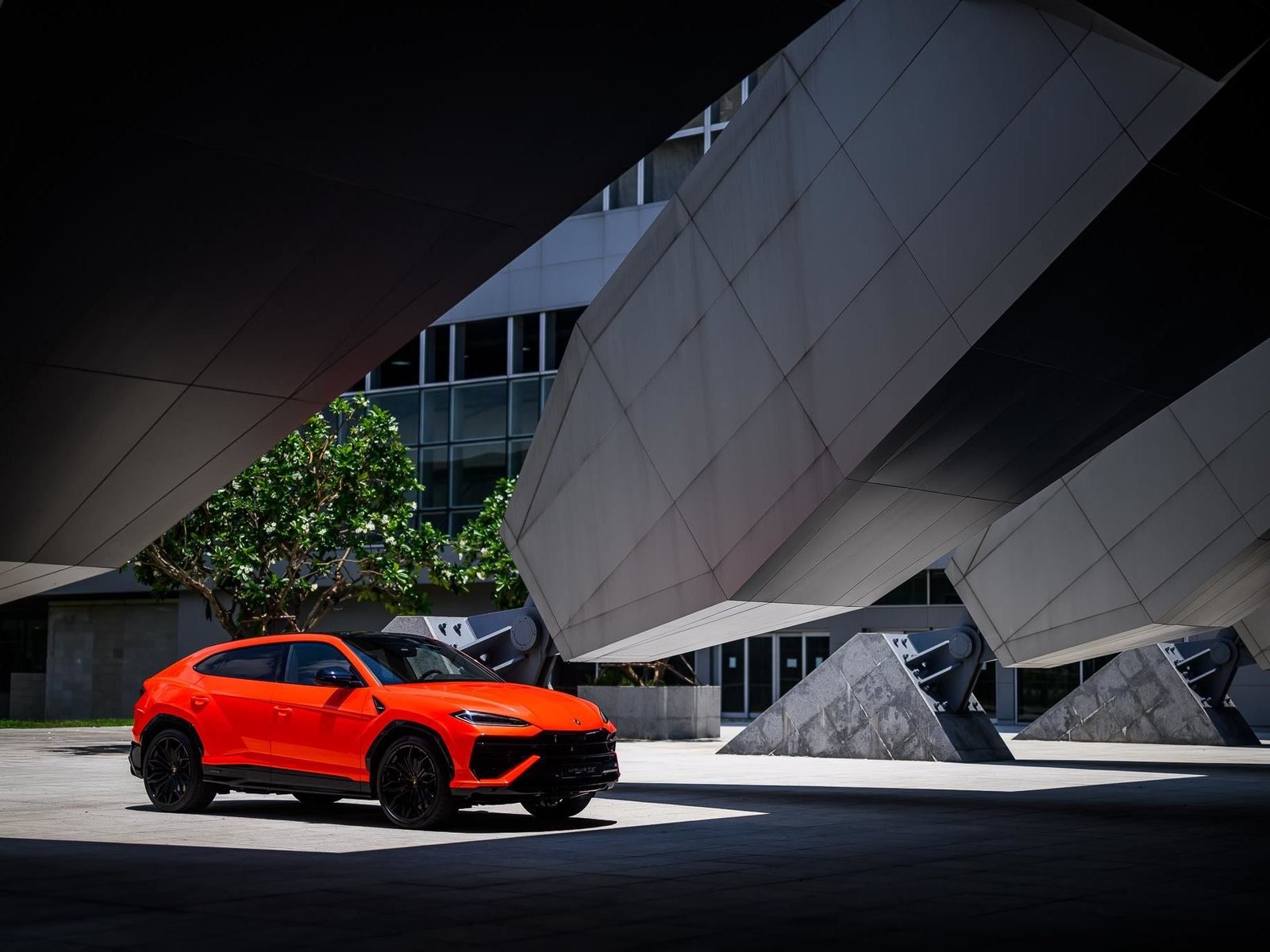 Orange Lamborghini Urus SE parked in a modern architectural setting, showcasing its aggressive front fascia and new floating hood design