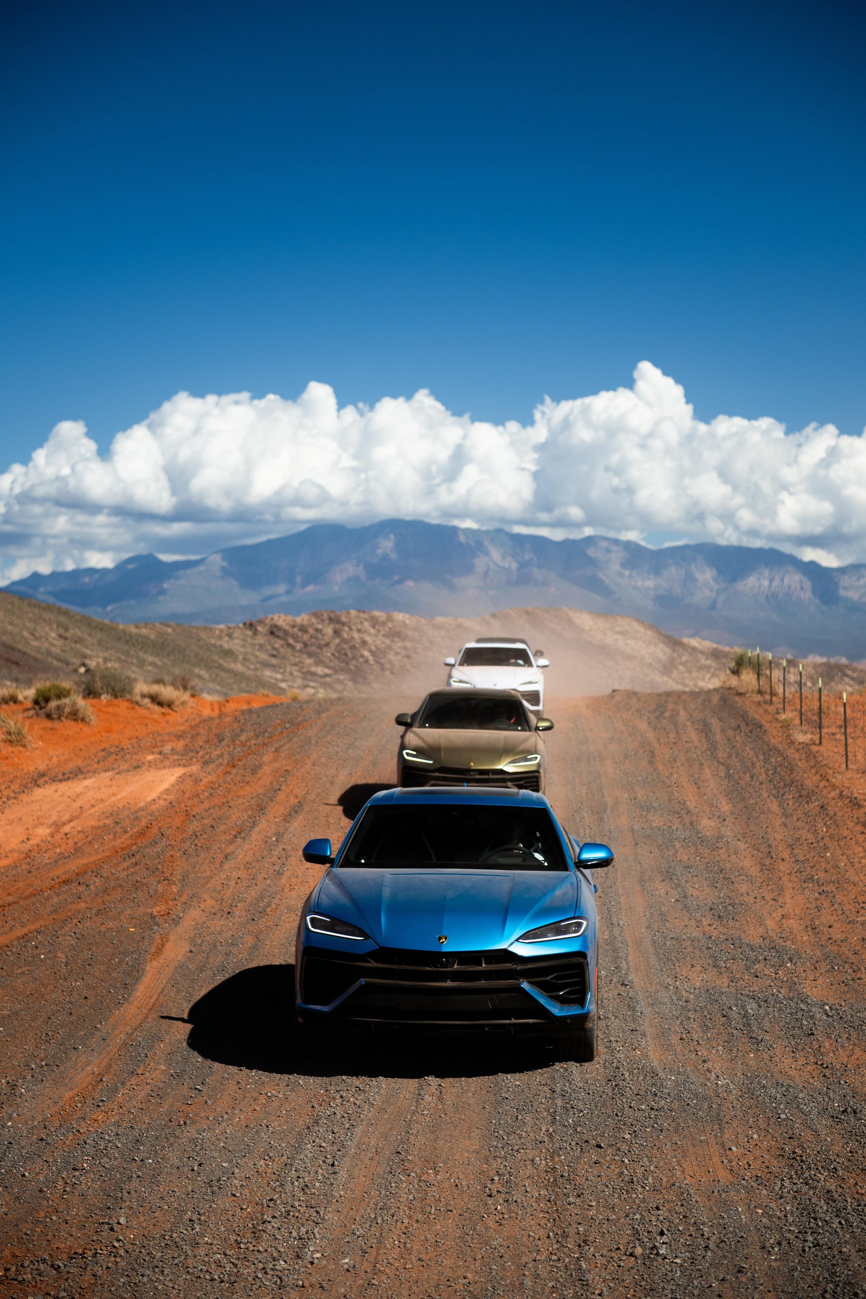 Lamborghini Sent A Convoy Of Urus Ses Into Zion'S Desert. The Real Destination Was Brand Loyalty. 3 Convoy of colorful lamborghini urus se suvs driving on a dusty reddish gravel road under blue sky