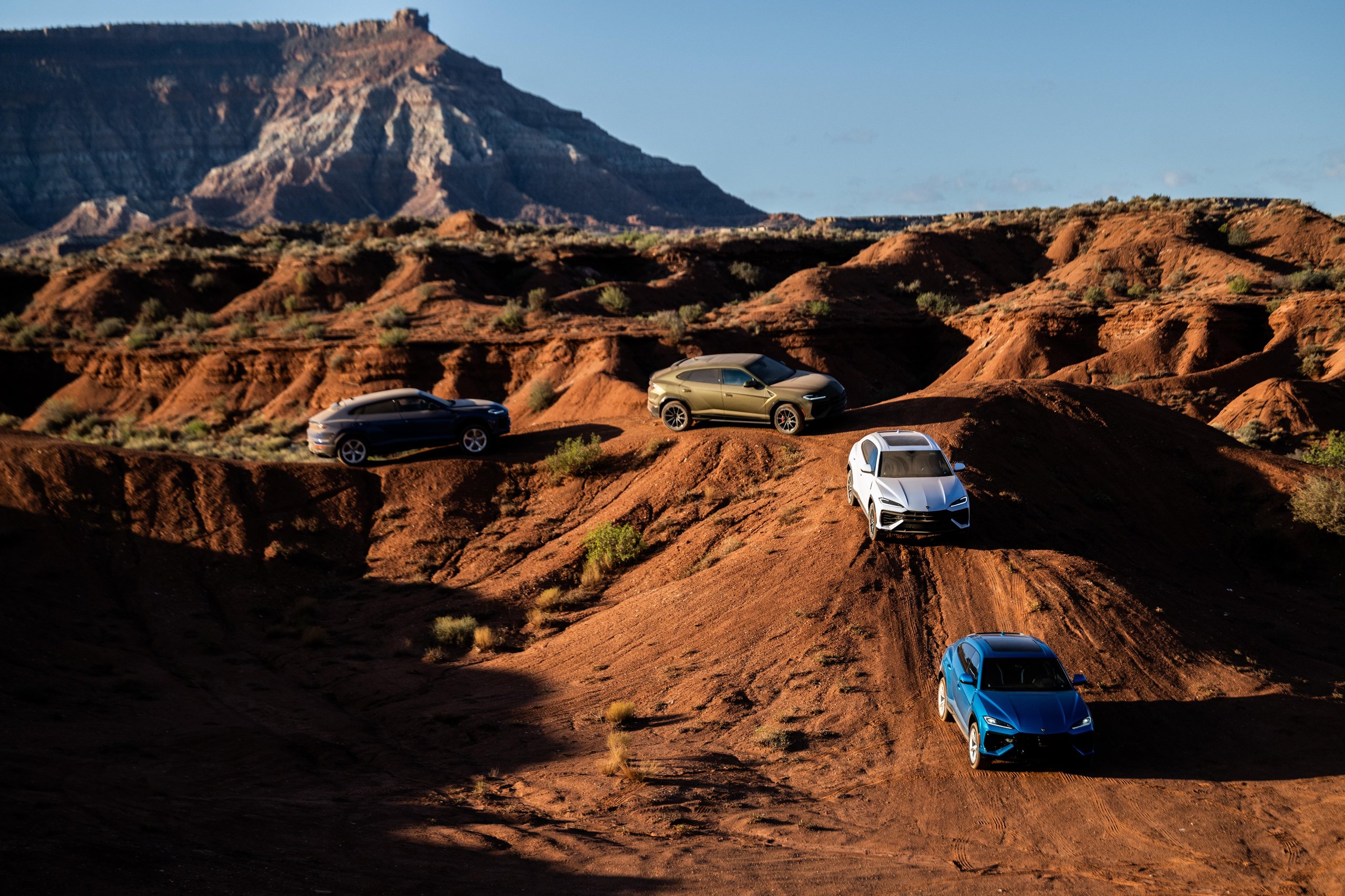 Lamborghini Sent A Convoy Of Urus Ses Into Zion'S Desert. The Real Destination Was Brand Loyalty. 9 Multiple lamborghini urus se vehicles in various colors positioned on rugged reddish-brown desert terrain with a mountain in the background