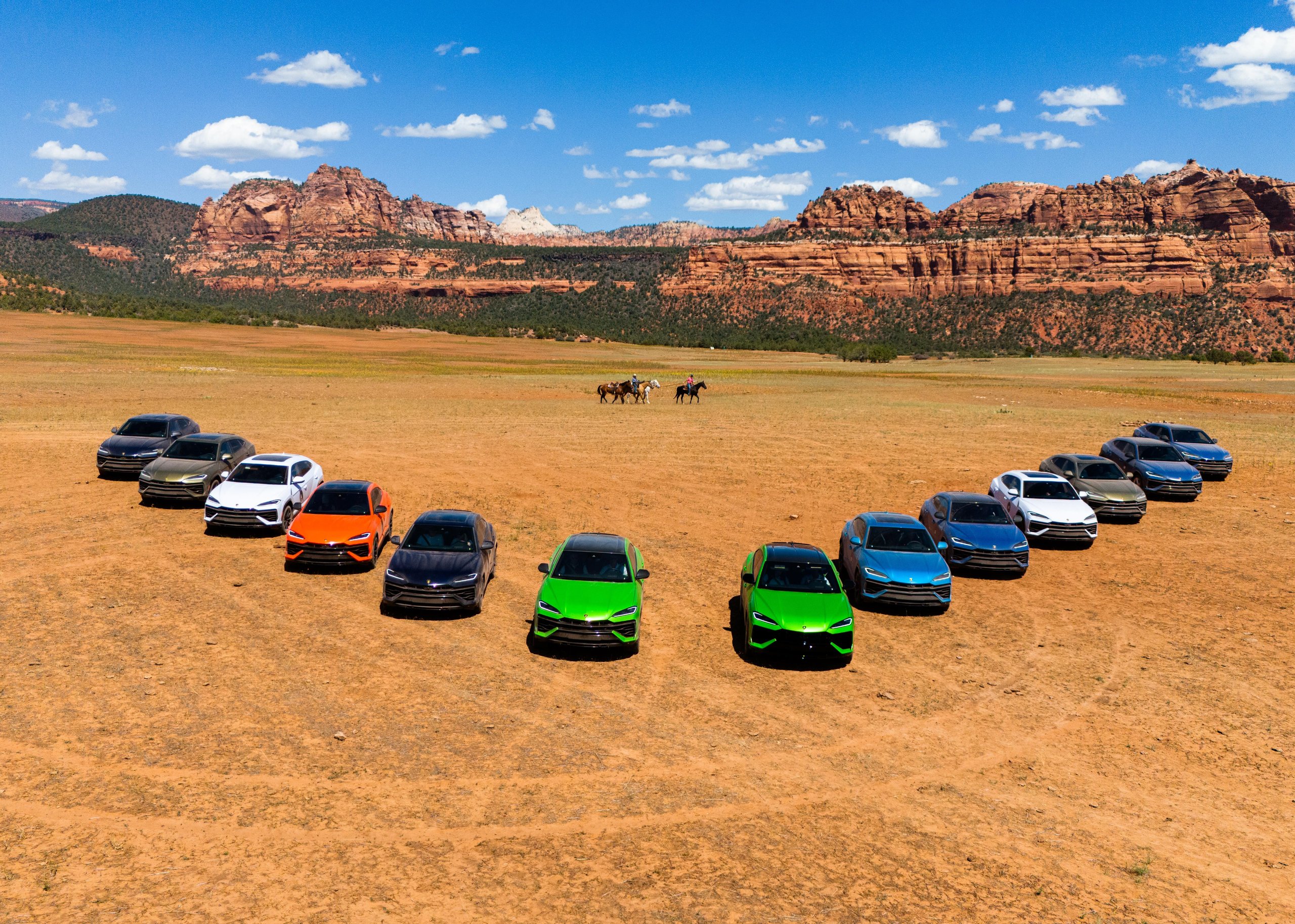 Lamborghini Sent A Convoy Of Urus Ses Into Zion'S Desert. The Real Destination Was Brand Loyalty. 11 Aerial view of lamborghini urus se fleet in v-formation on desert field with red rock mountains and horseback riders in background
