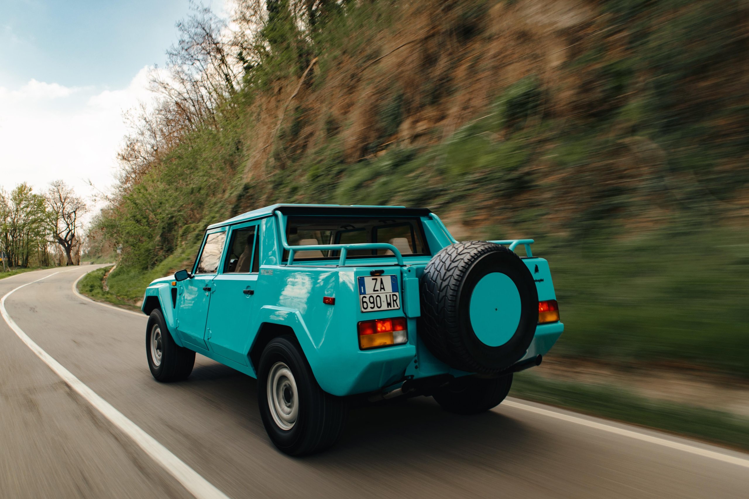 From Rambo Lambo To 800 Cv Hybrid: How Lamborghini Spent Half A Century Building The World'S Most Extreme Suv 3 A teal lamborghini lm002 captured in motion from the rear three-quarter angle on a winding road