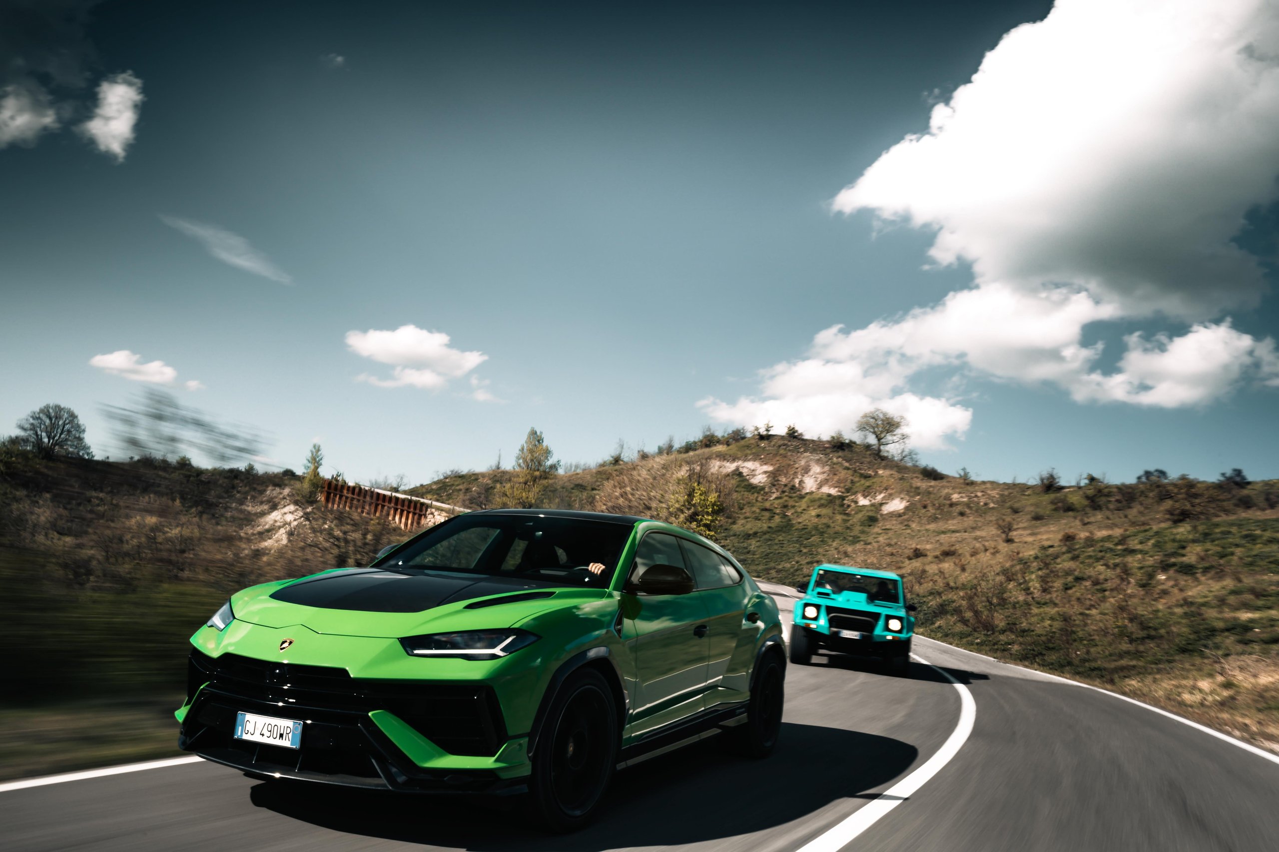 From Rambo Lambo To 800 Cv Hybrid: How Lamborghini Spent Half A Century Building The World'S Most Extreme Suv 7 A vibrant green lamborghini urus performing a dynamic turn on a winding mountain road with a teal lamborghini lm002 following closely behind