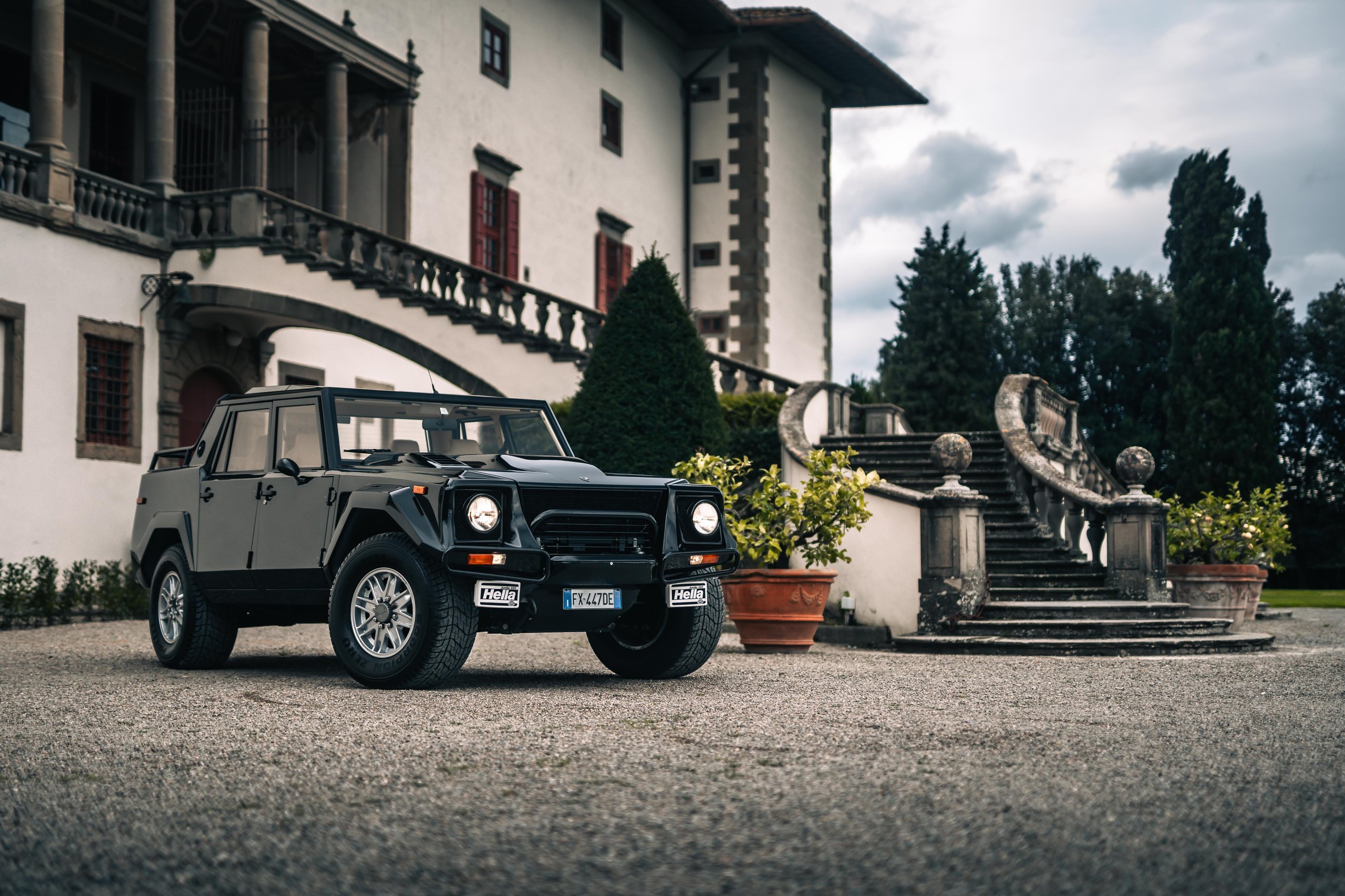 From Rambo Lambo To 800 Cv Hybrid: How Lamborghini Spent Half A Century Building The World'S Most Extreme Suv 5 A black lamborghini lm002 parked on a gravel driveway in front of a grand historic building with classical architecture