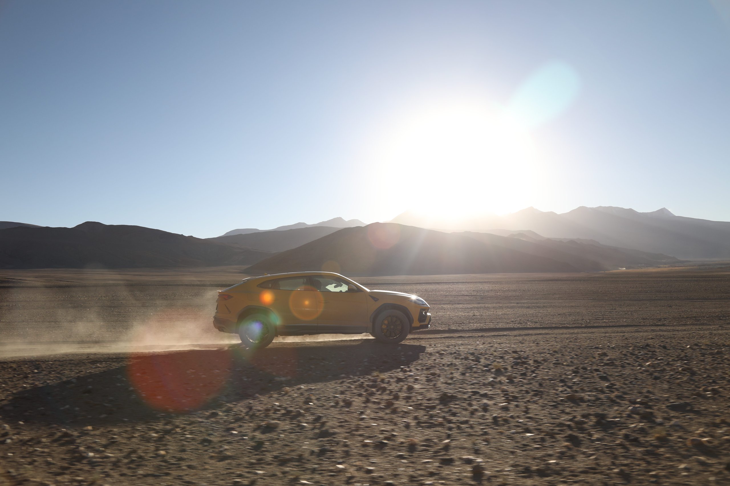The Lamborghini Urus At 19,300 Feet: Conquering The World'S Highest Drivable Road 3 Yellow lamborghini urus kicking up dust on a barren rocky landscape with mountains in the background