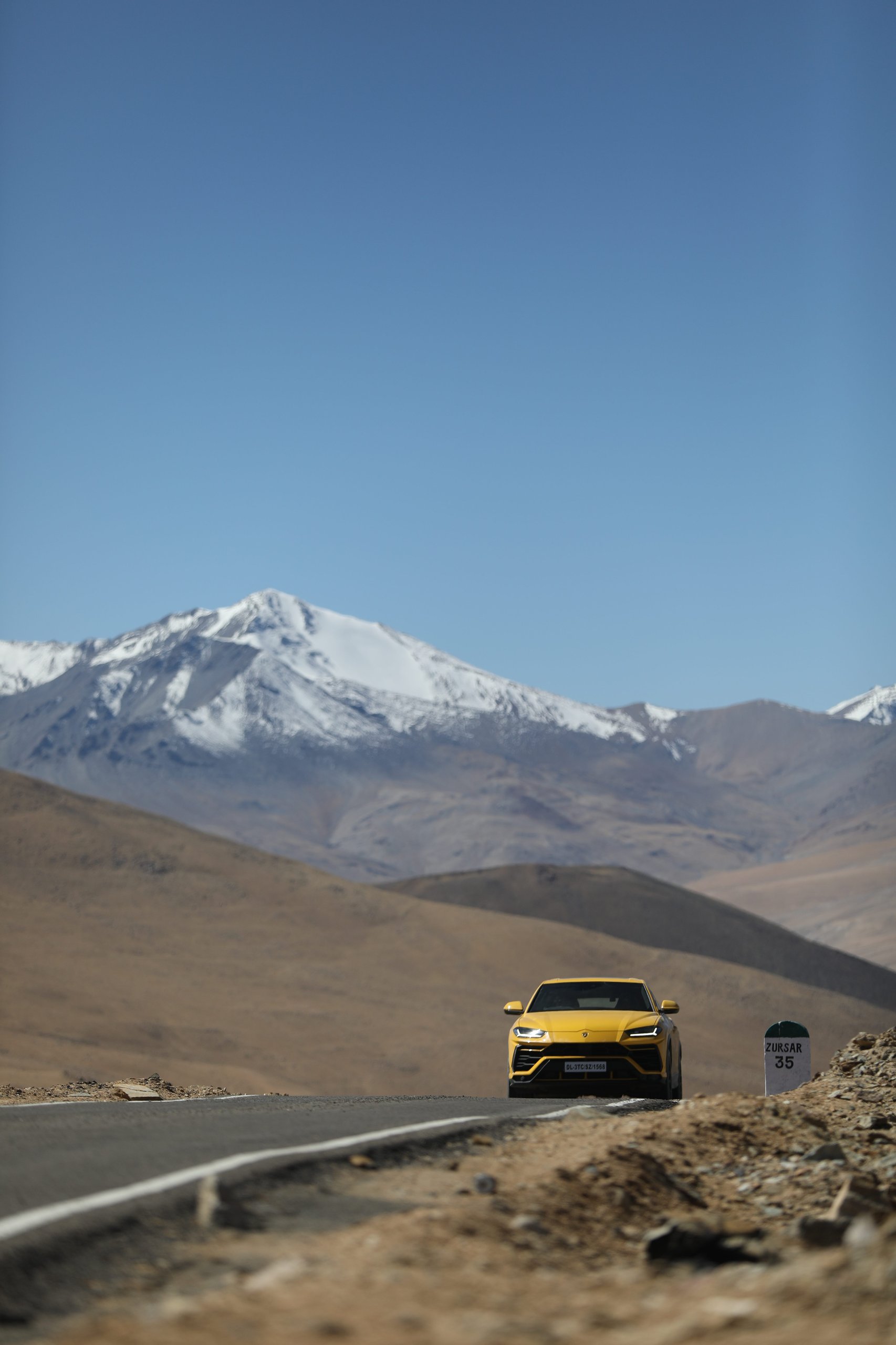 The Lamborghini Urus At 19,300 Feet: Conquering The World'S Highest Drivable Road 5 Yellow lamborghini urus on a straight mountain road with snow-capped peaks in the background